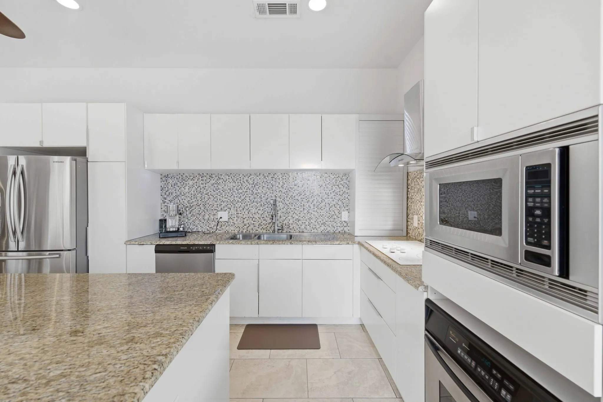 White cabinetry with stainless steel appliances, granite countertops, built-in microwave, and tile backsplash