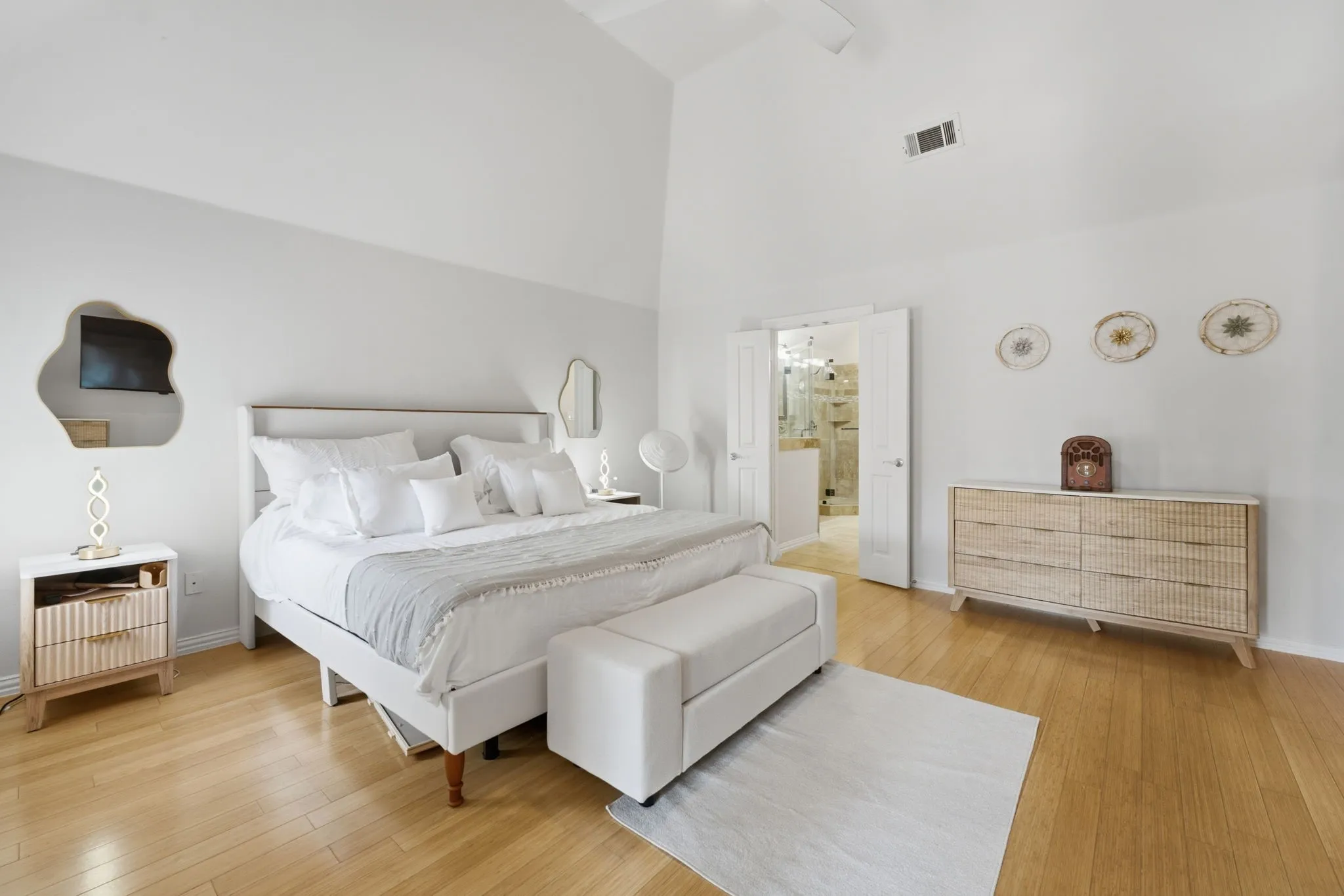 Vaulted ceiling, light wood-finish flooring, white double doors, and an attached full bathroom