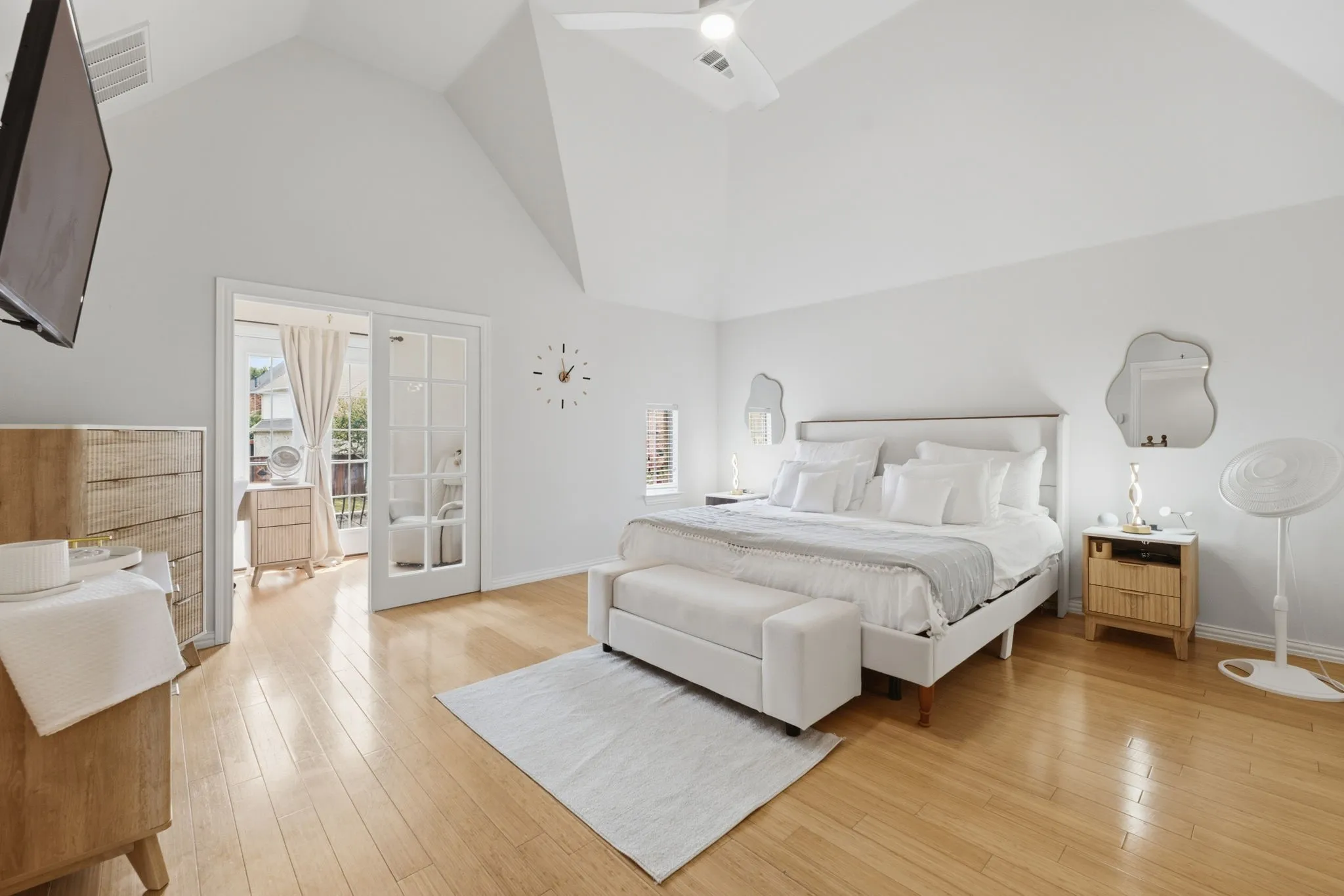 Vaulted ceiling, ceiling fan, wood-finish flooring, French doors, and a built-in wall-mounted television