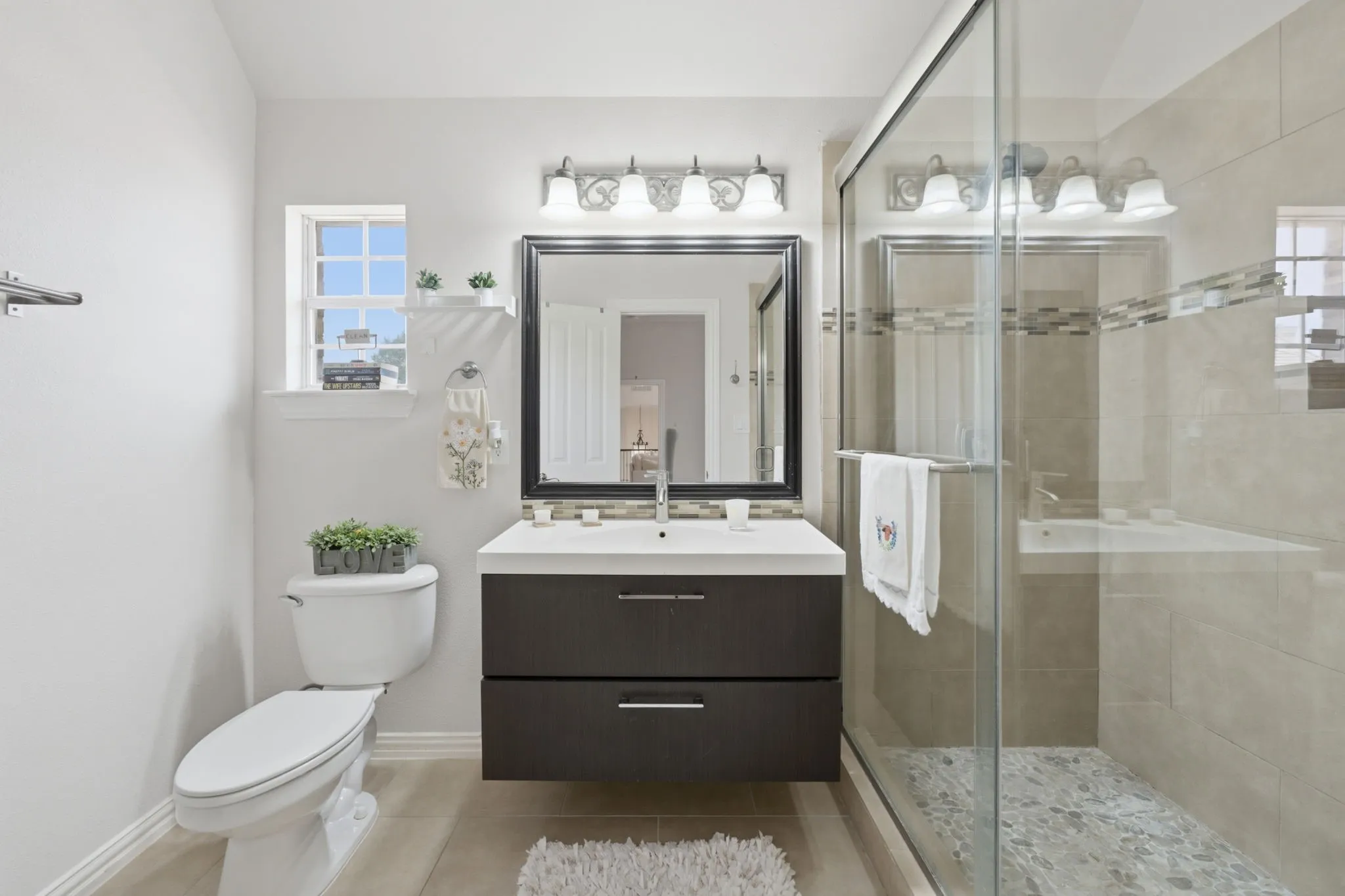 Floating vanity with integrated sink, modern framed mirror, glass-enclosed shower with tiled walls, and pebble flooring