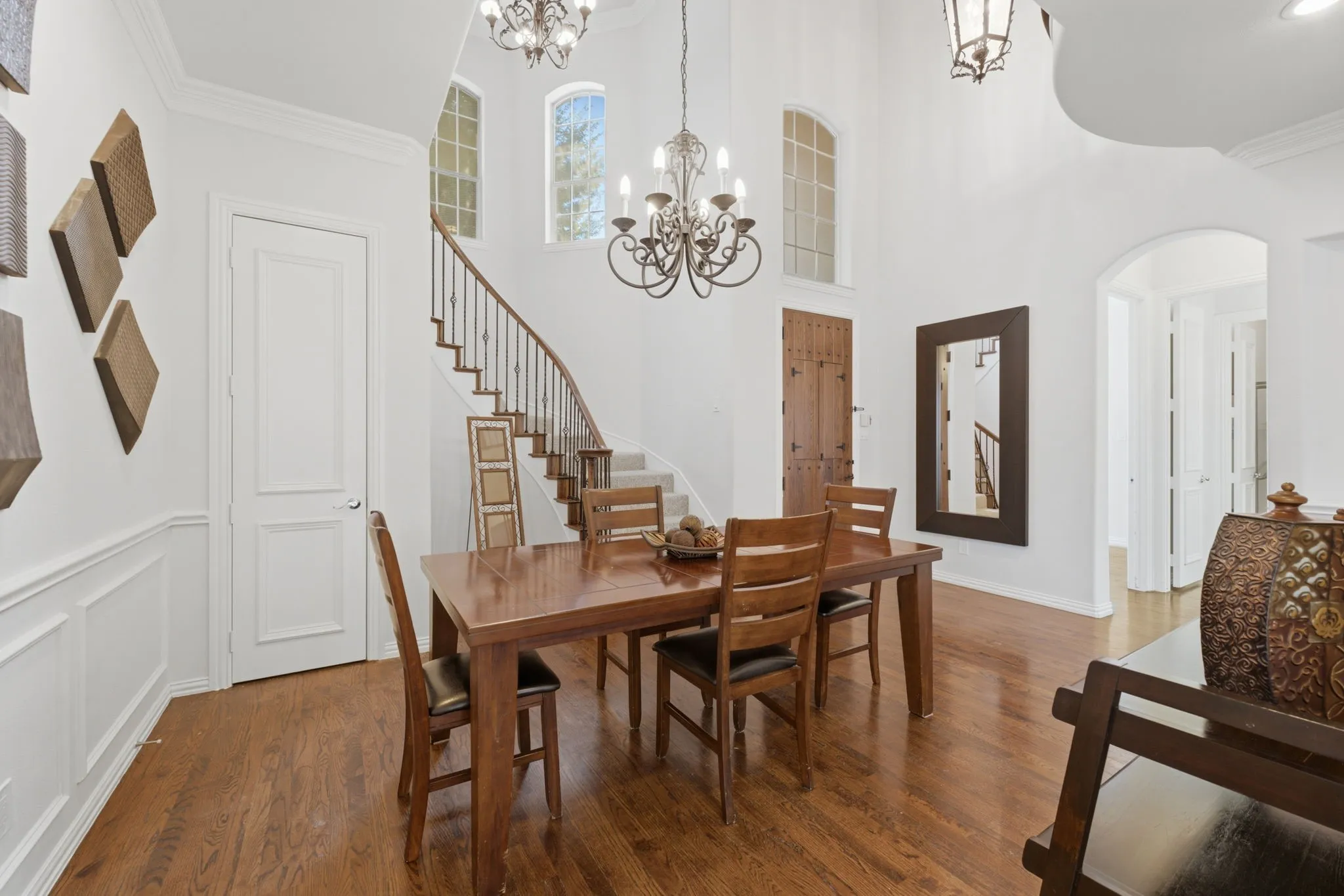 Vaulted ceiling with decorative chandelier, hardwood flooring, curved staircase with wrought iron railing, arched doorways, and wainscoting