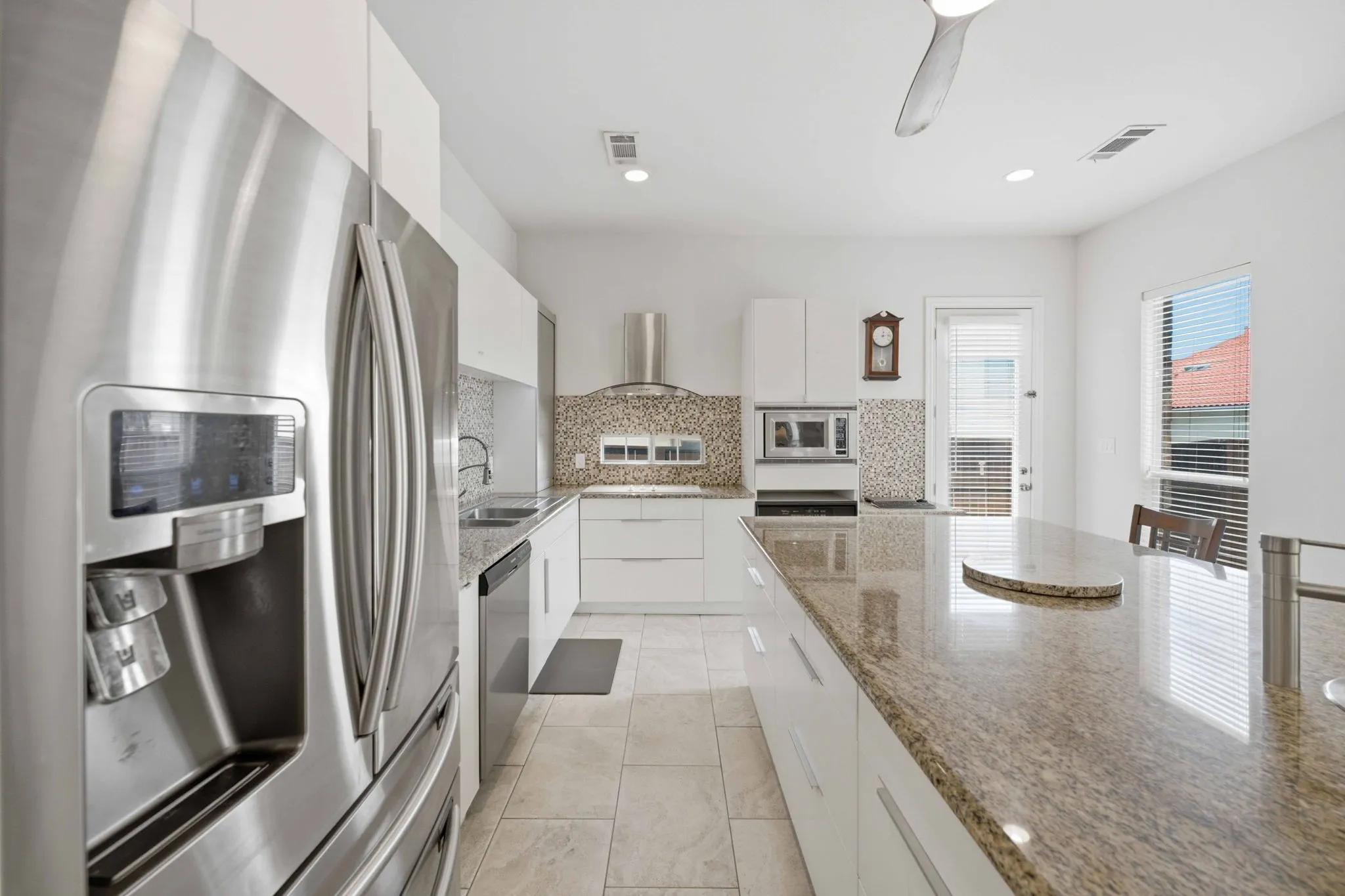 Kitchen featuring stainless steel appliances, white flat-panel cabinetry, light-toned tile flooring, granite countertops, and a decorative tile backsplash