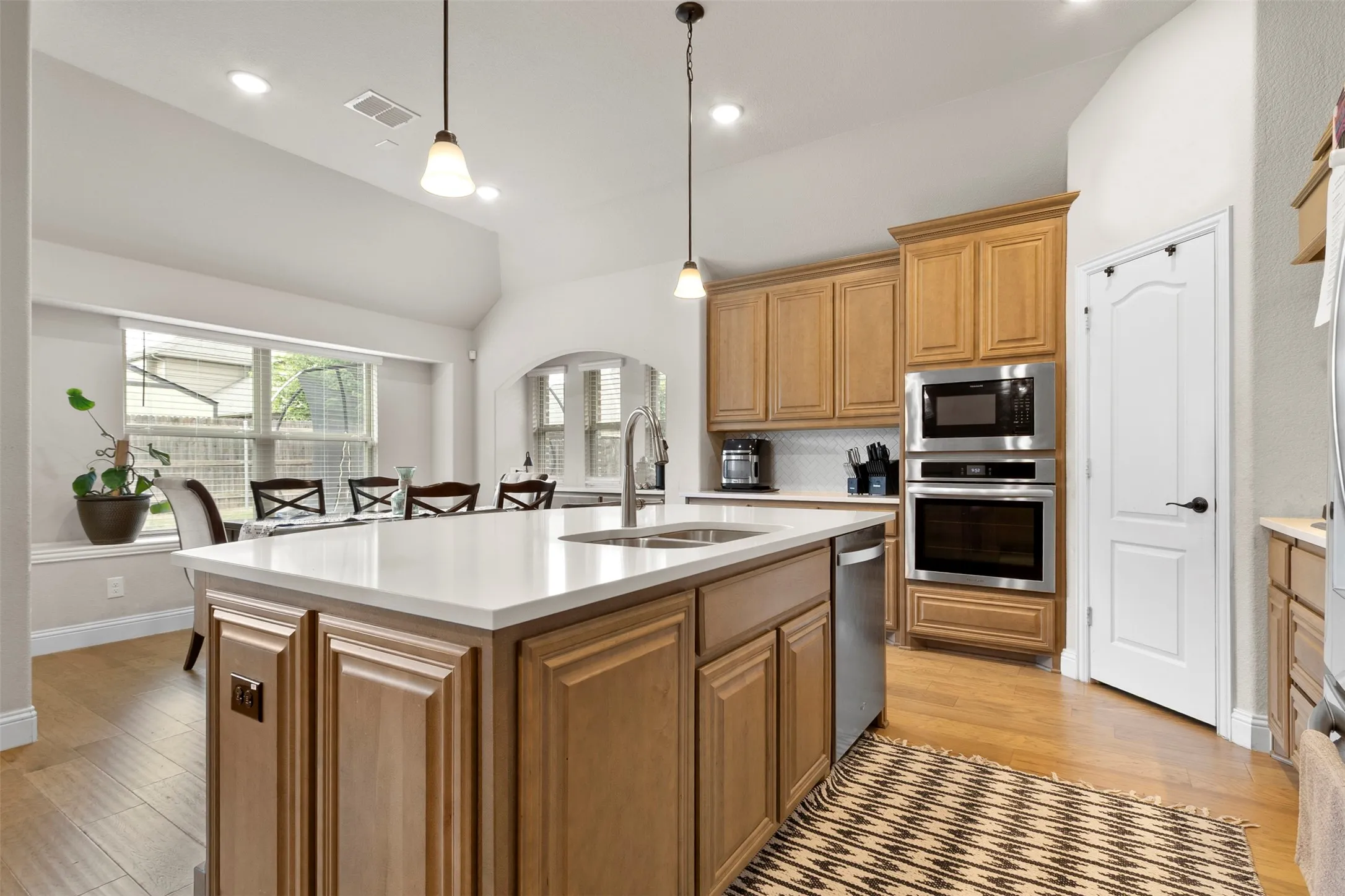 Kitchen island with a white countertop and integrated sink, stainless steel appliances, wood-finish flooring, and light wood cabinetry