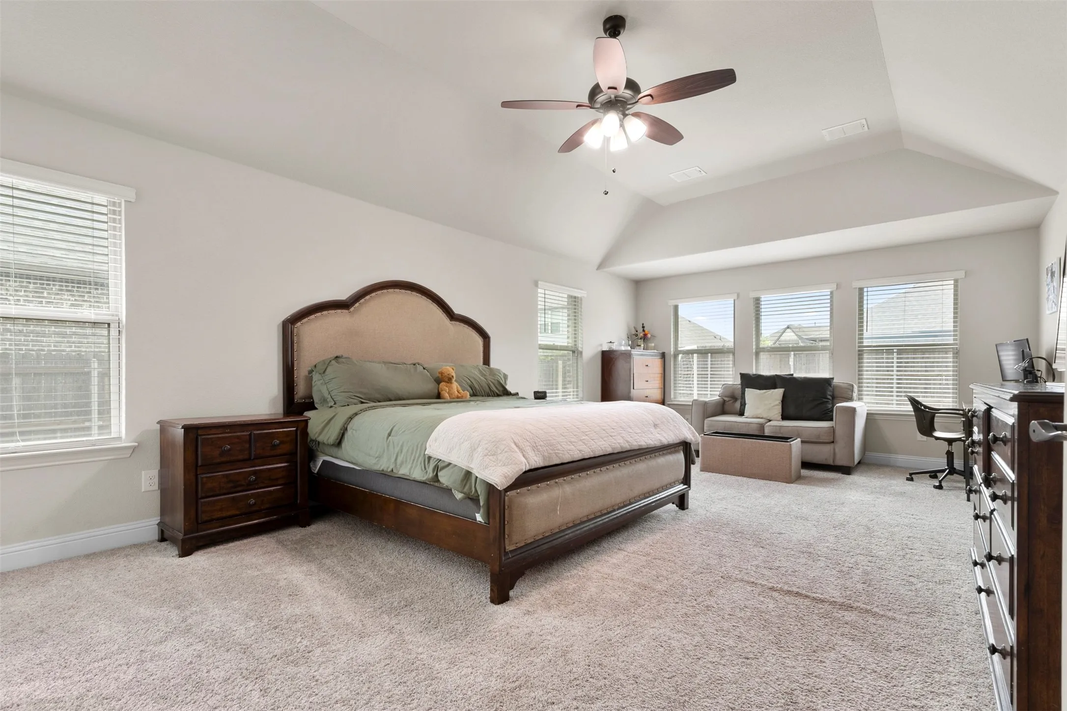 Vaulted ceiling with a ceiling fan, multiple windows with blinds, and light-colored carpeting