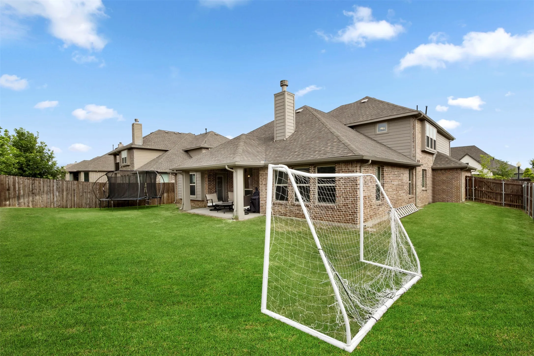 Expansive backyard featuring a brick exterior, covered patio, and wood privacy fencing