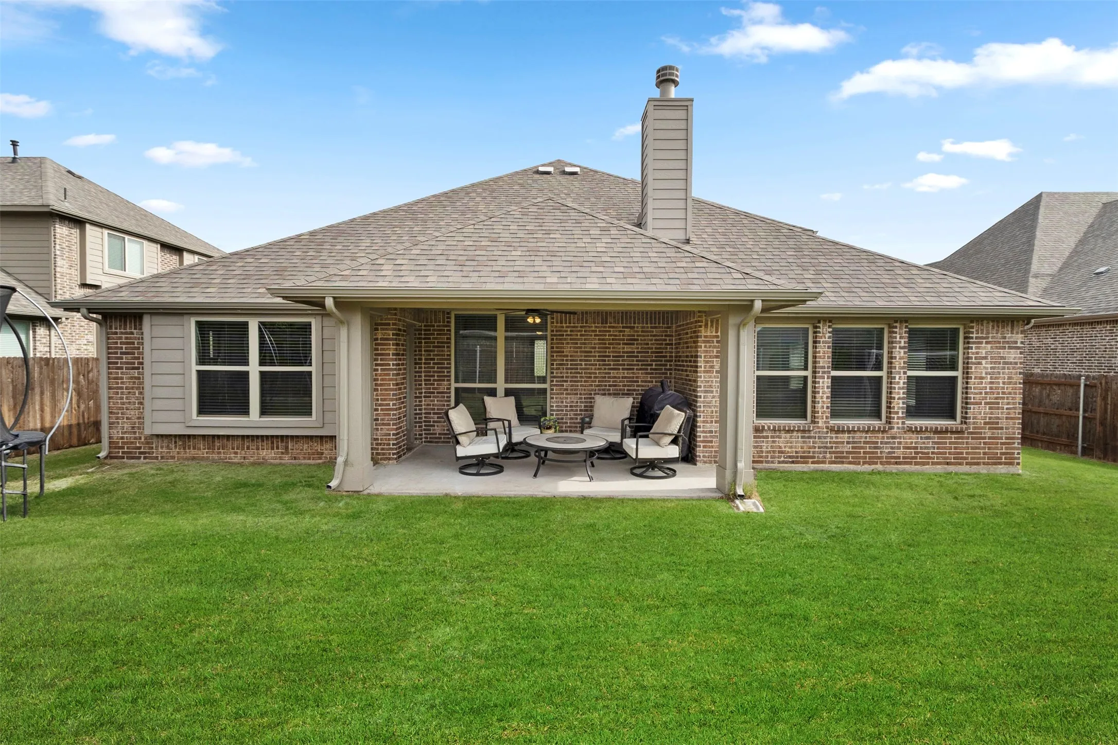 Expansive lawn with a covered concrete patio, brick exterior, vinyl siding accents, and a shingled roof