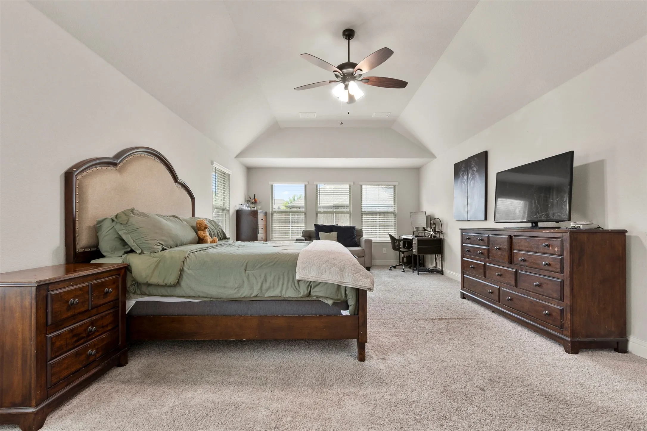 Vaulted ceiling with a ceiling fan, neutral carpeting, and multiple windows