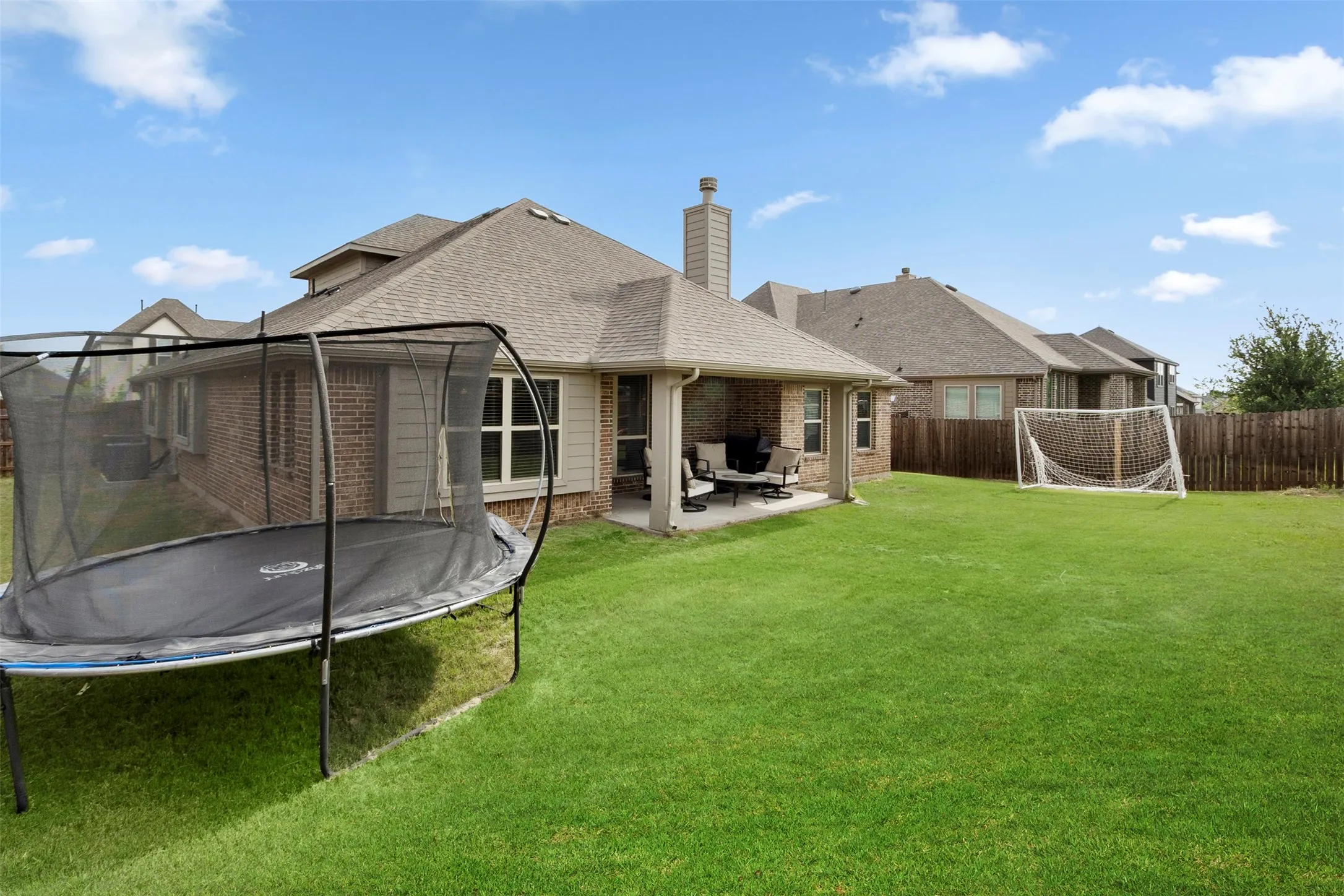 Expansive backyard featuring a lush lawn, brick exterior, covered patio, and a privacy fence