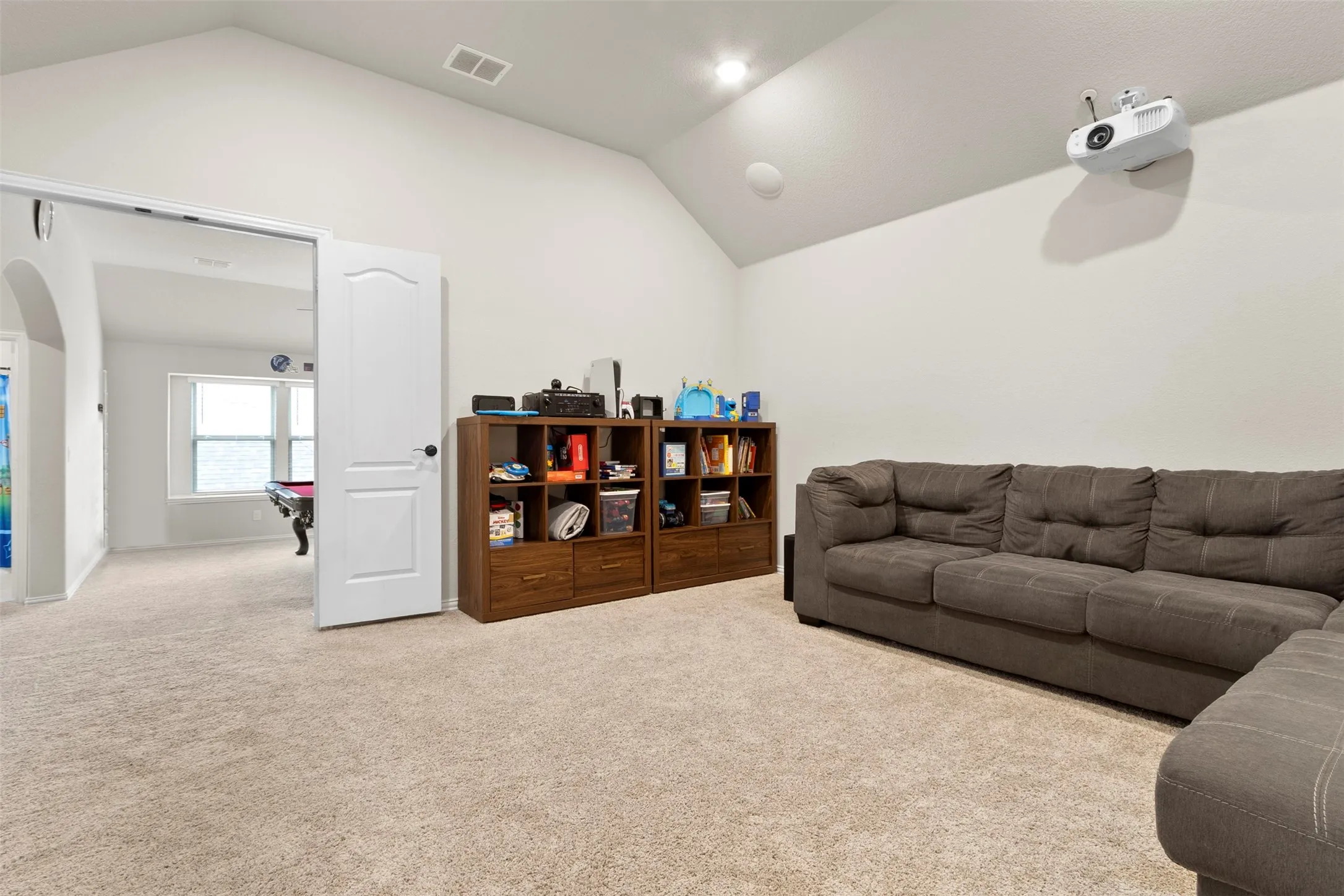 Vaulted ceiling, recessed lighting, wall-mounted projector, wall-to-wall carpeting, and barn door entry