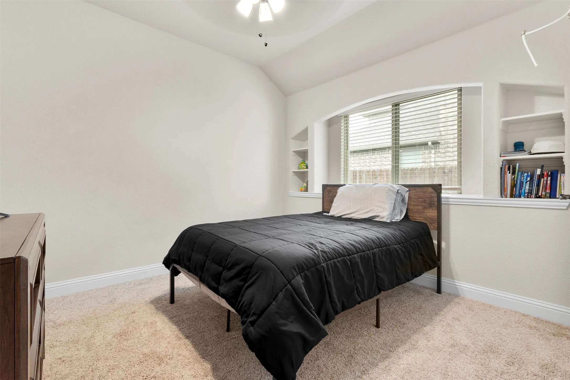Vaulted ceiling with a ceiling fan, arched window with blinds, built-in shelving, built-in wall niches, and carpet flooring