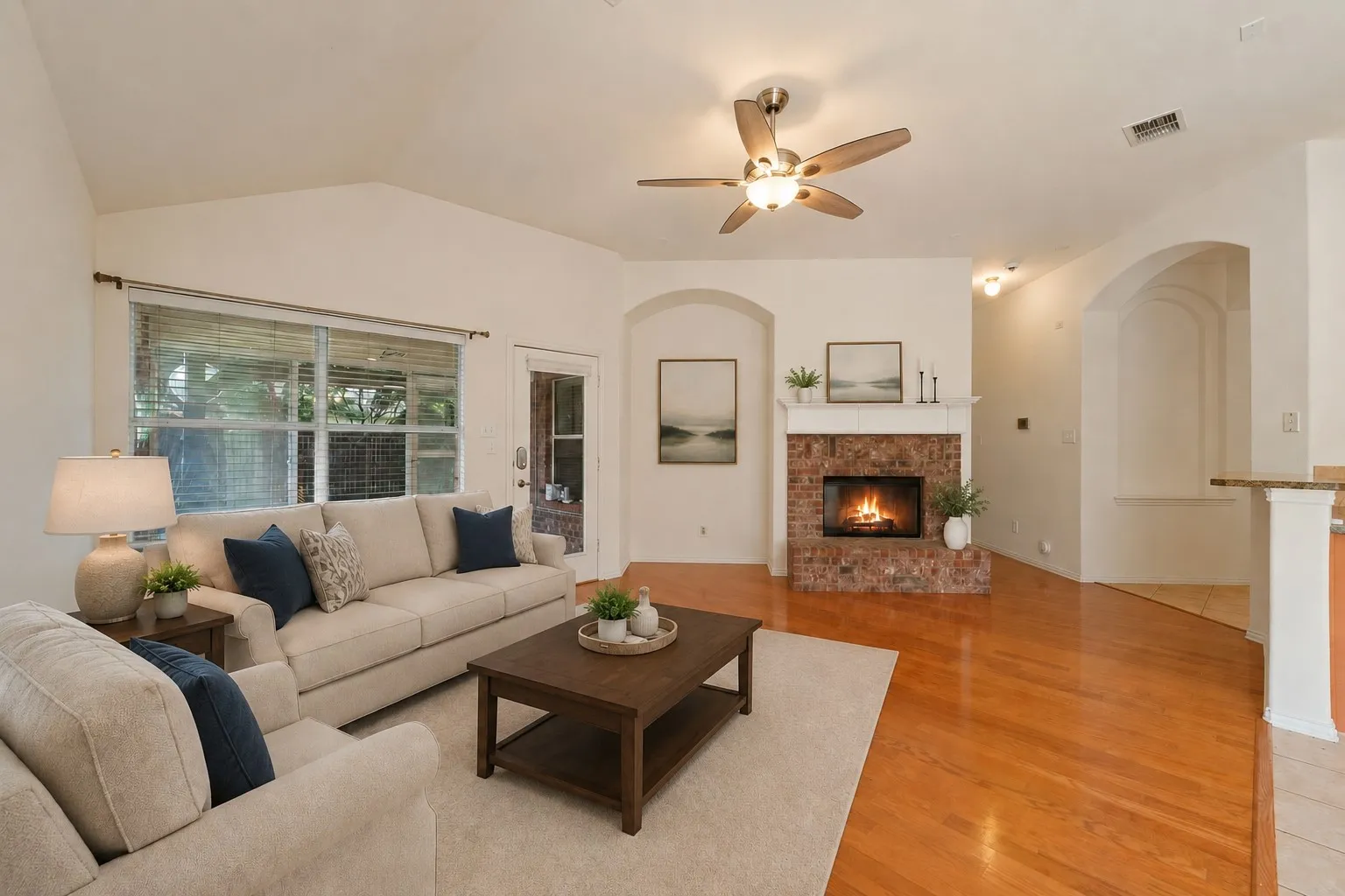Living area featuring vaulted ceilings, wood-finish flooring, a brick fireplace with a mantel, and an overhead ceiling fan