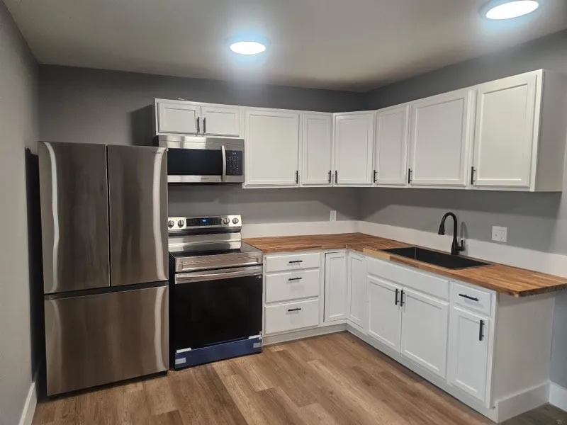 Kitchen featuring stainless steel appliances, white cabinetry with dark hardware, butcher block countertops, a black sink, and wood-finish flooring