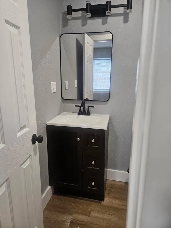 Bathroom featuring a dark wood-finish vanity with integrated sink, matte black faucet, framed mirror, and modern three-light fixture