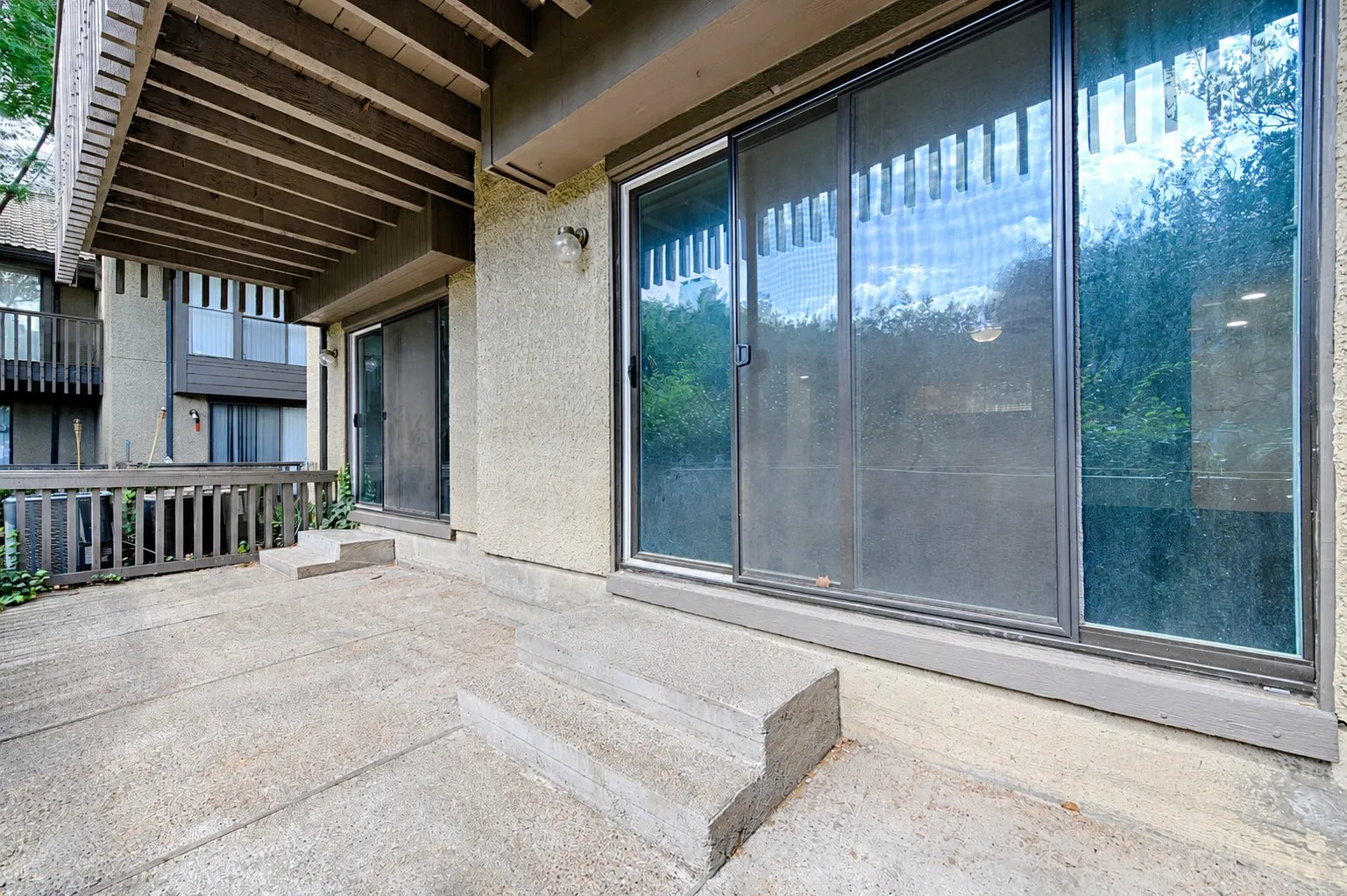 Private concrete patio with steps, featuring a sliding glass door, an additional exterior door, and an overhead balcony