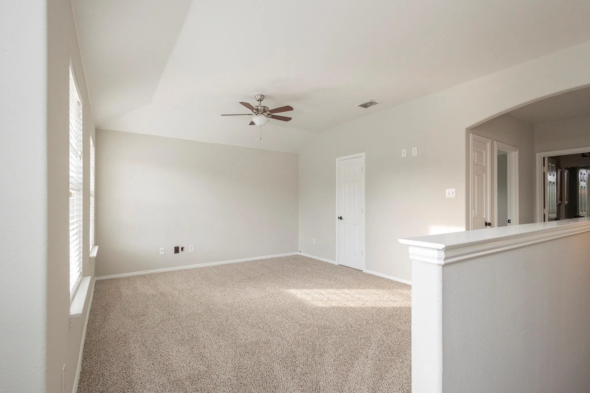 Carpeted room featuring a tray ceiling, ceiling fan, multiple windows with blinds, and an arched doorway