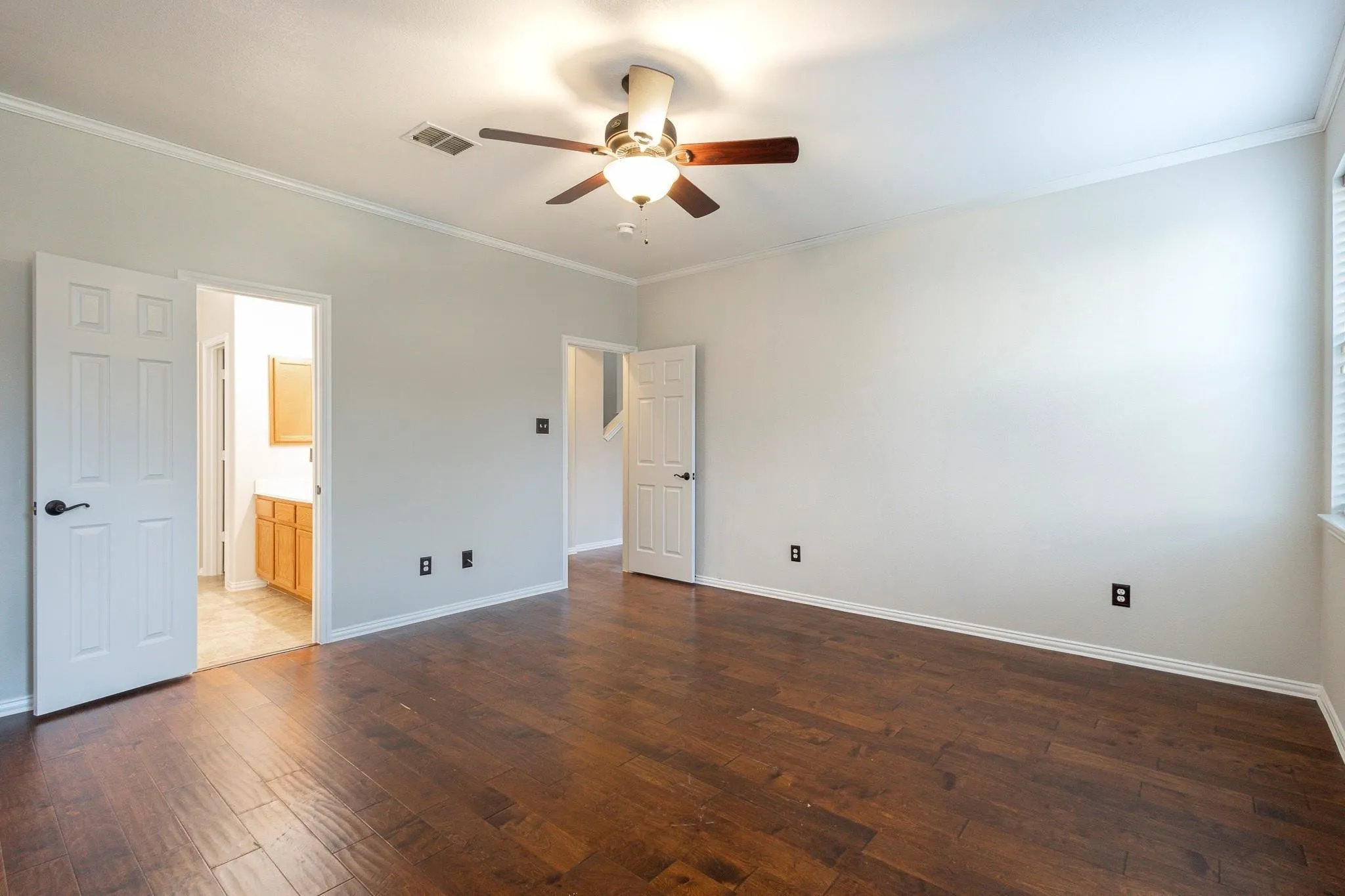 Spacious room featuring wood-finish flooring, white trim details, and overhead ceiling fan with lighting