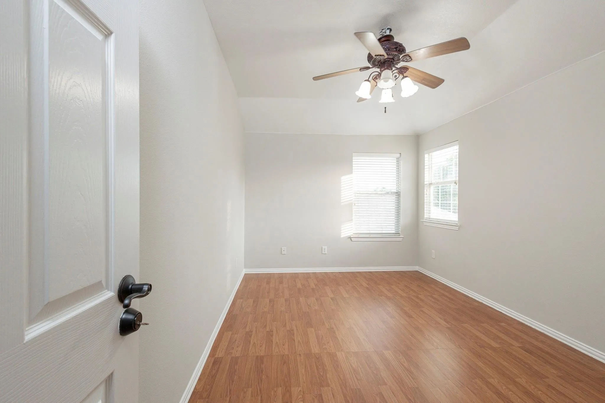 Tray ceiling with a ceiling fan light fixture, wood-finish flooring, and multiple windows with blinds