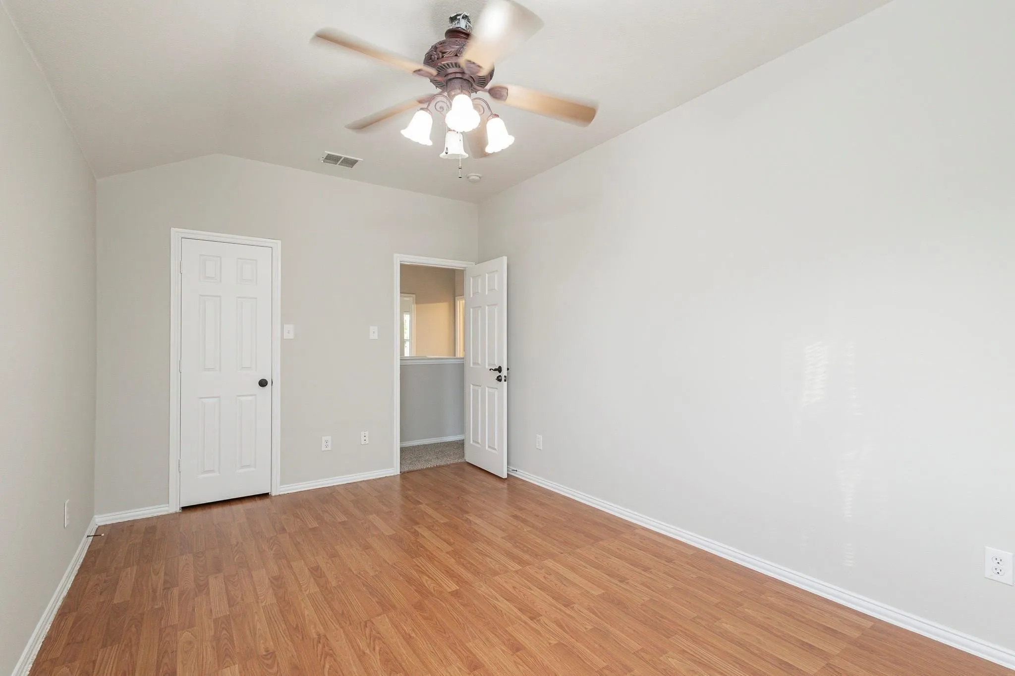Vaulted ceiling, wood-finish flooring, ceiling fan with integrated lighting, and white paneled doors