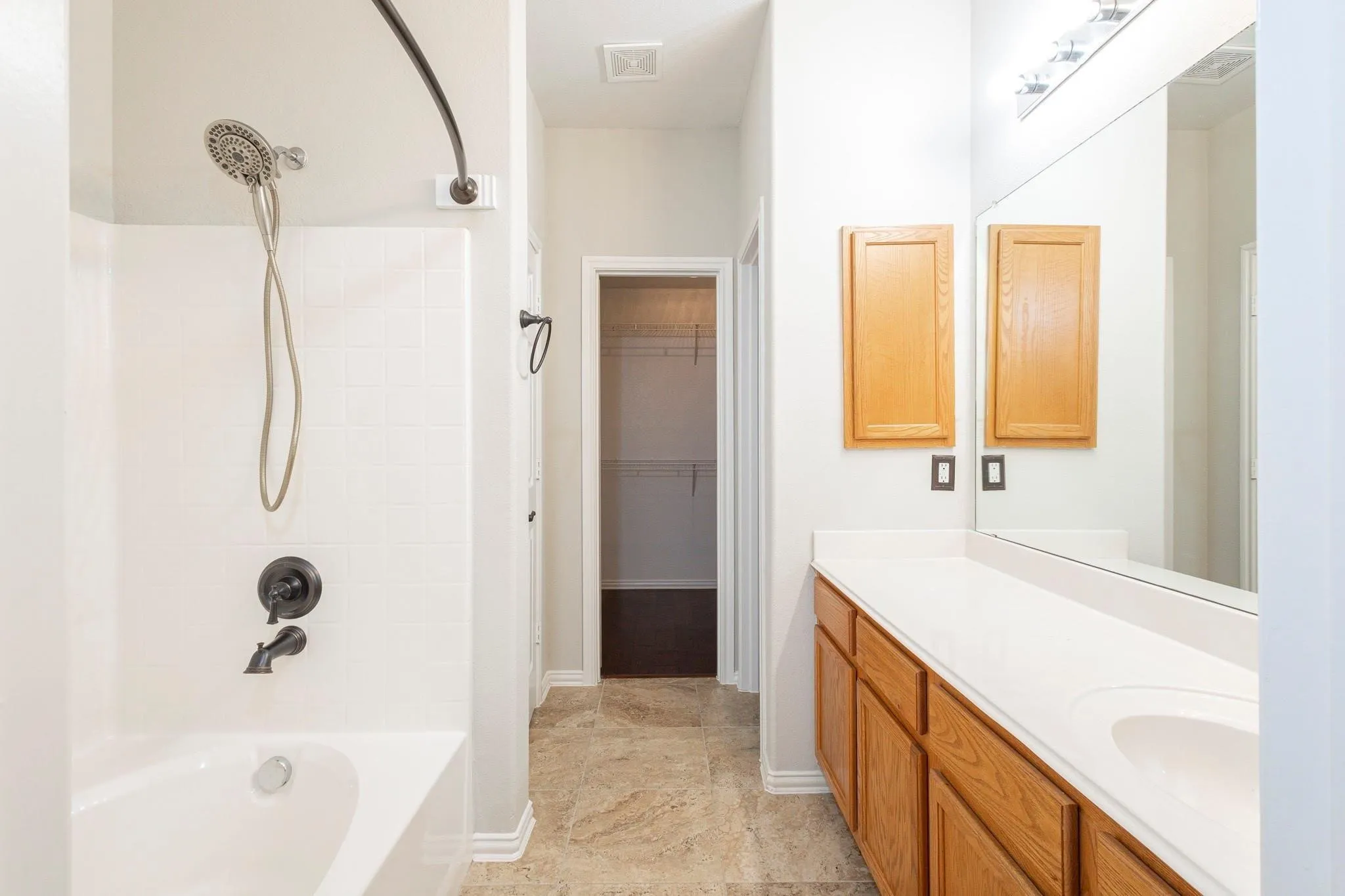 Bathroom featuring a bathtub with a shower system, a vanity with a single sink and light wood cabinetry, a large mirror, and tiled flooring