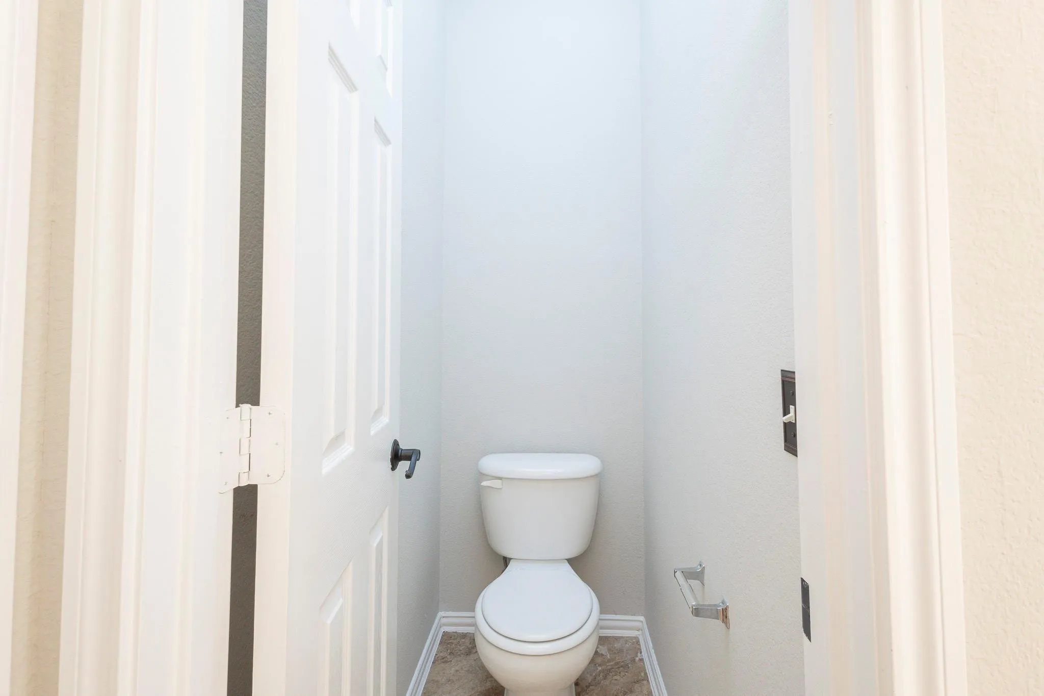 Recessed toilet alcove featuring a white toilet, neutral-toned flooring, and a paneled door with dark hardware