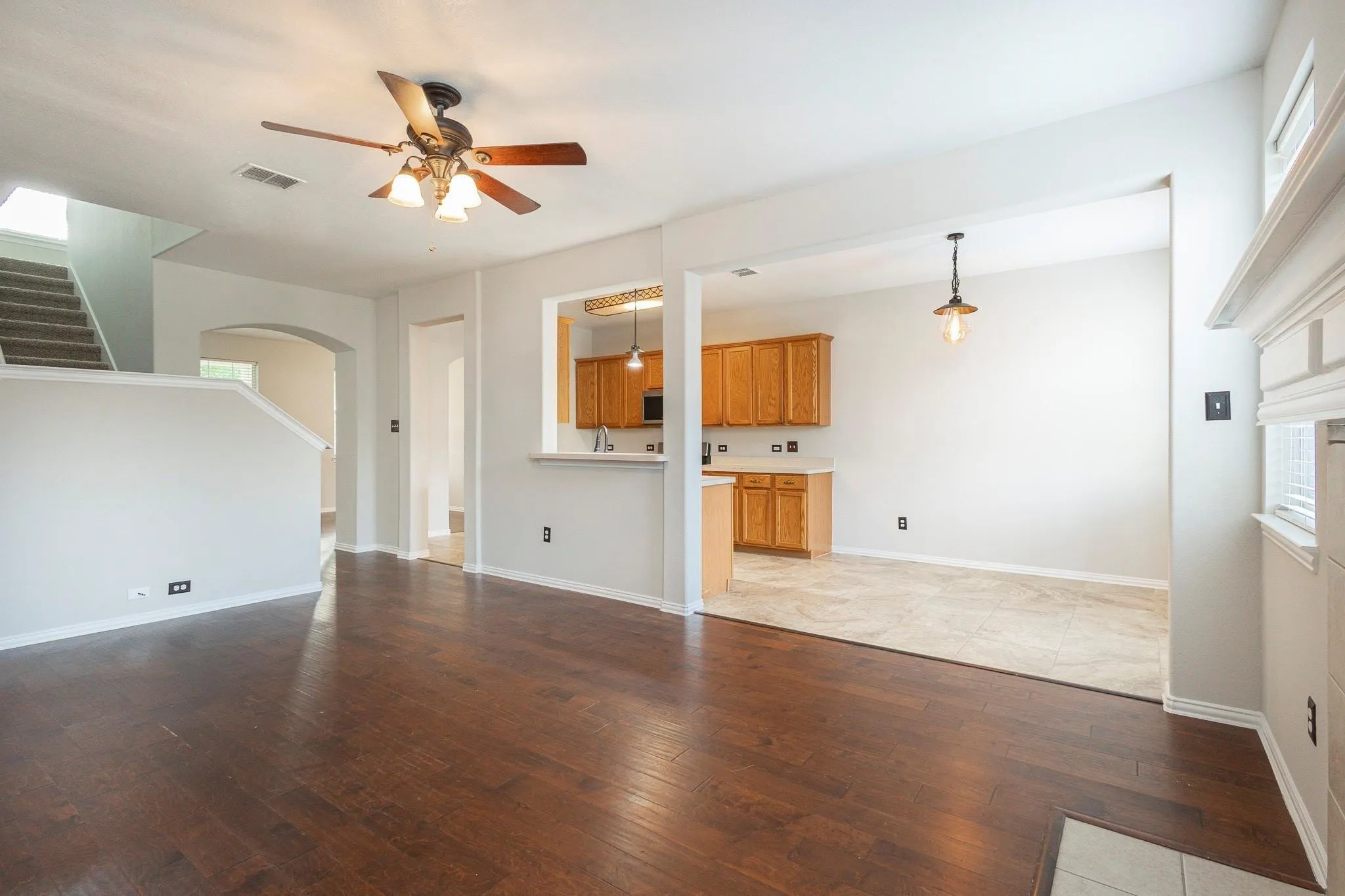 Dark wood-finish flooring, ceiling fan with integrated lighting, kitchen passthrough with lower cabinetry, light-toned wall paint, and white trim