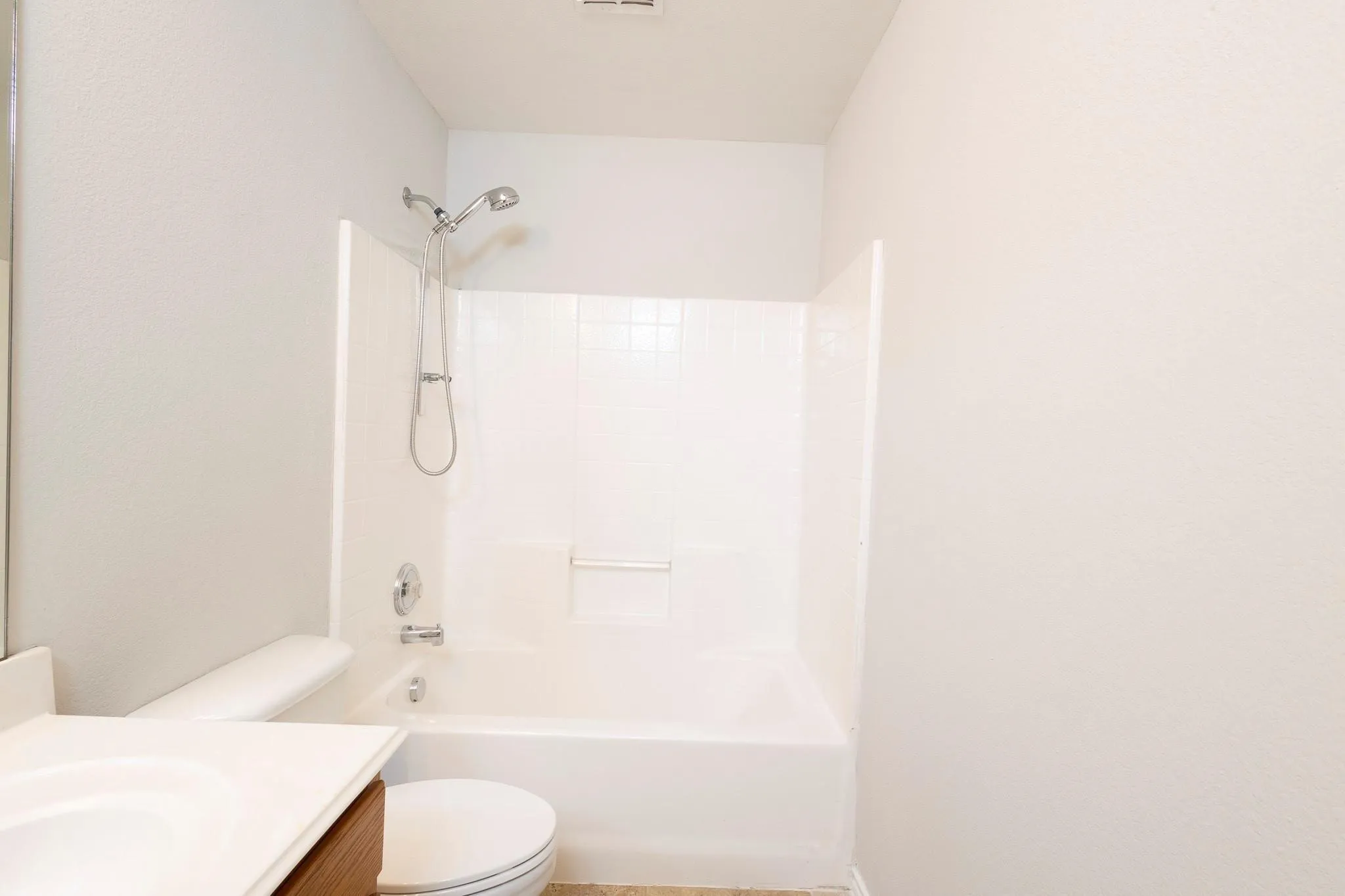 White bathtub with an integrated shower, chrome fixtures, and white tile surround