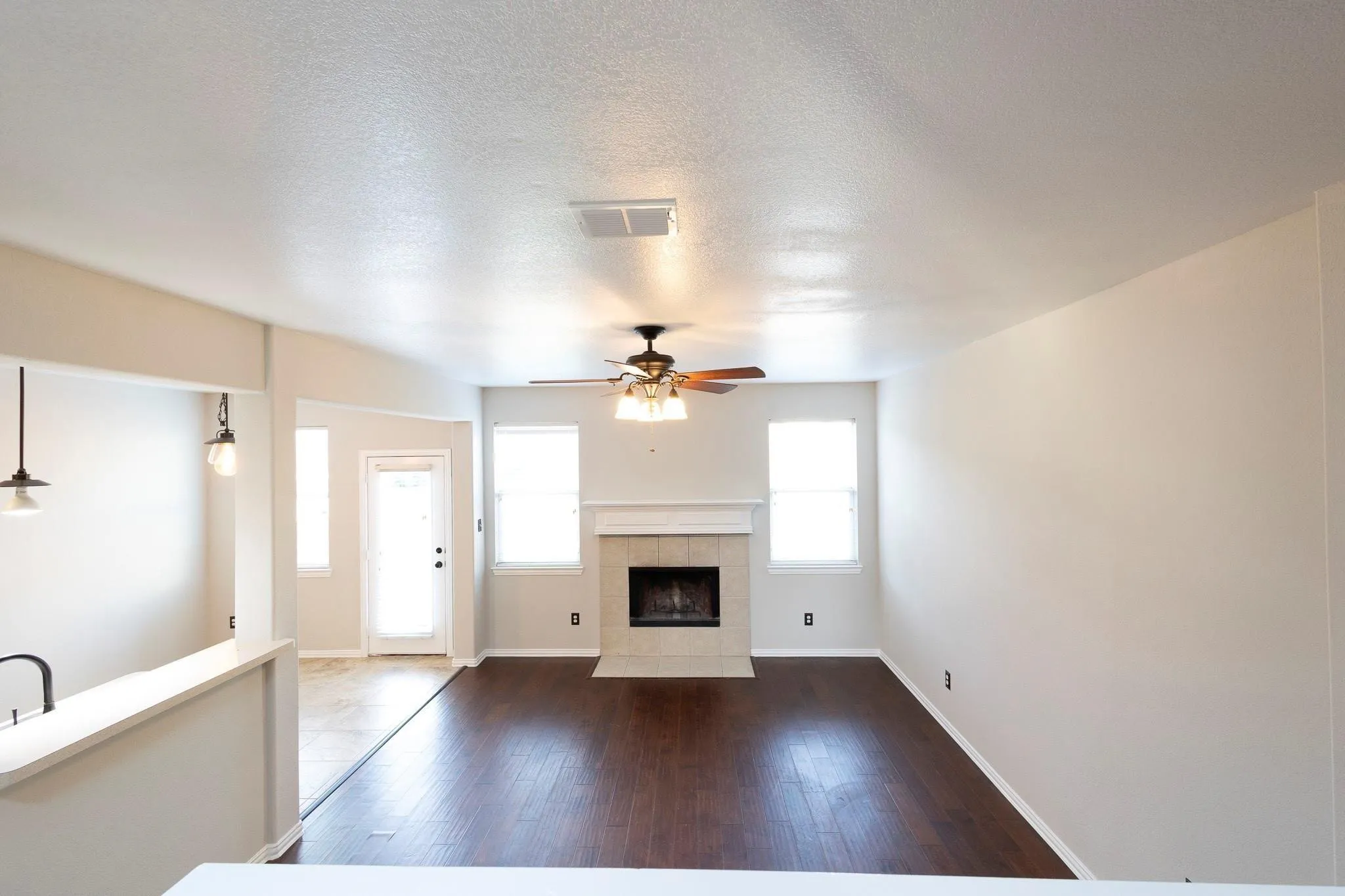 Spacious living area featuring wood-finish flooring, a fireplace with a mantel, multiple windows, an exterior door, and a ceiling fan