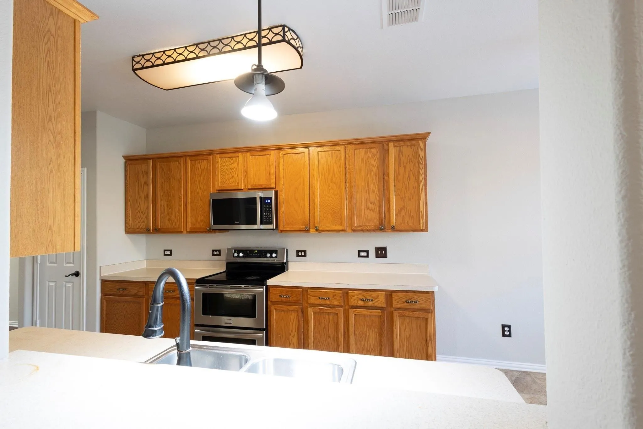 Kitchen with wood cabinetry, stainless steel appliances, dual basin sink, and pendant lighting