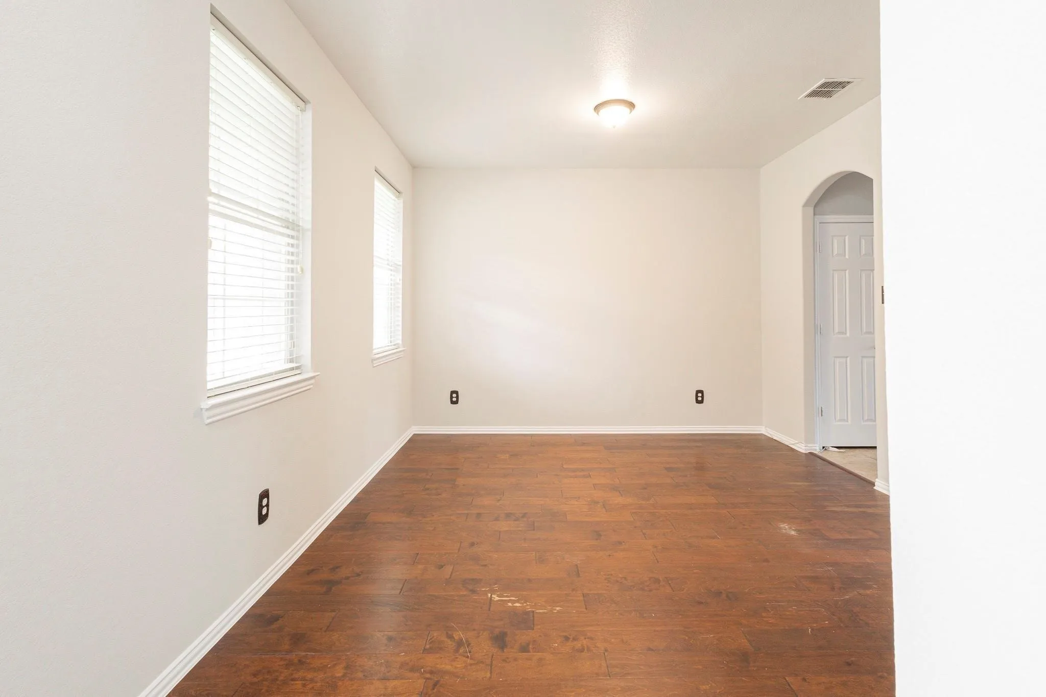 Wood-finish flooring with white baseboards, multiple windows with horizontal blinds, and an arched doorway