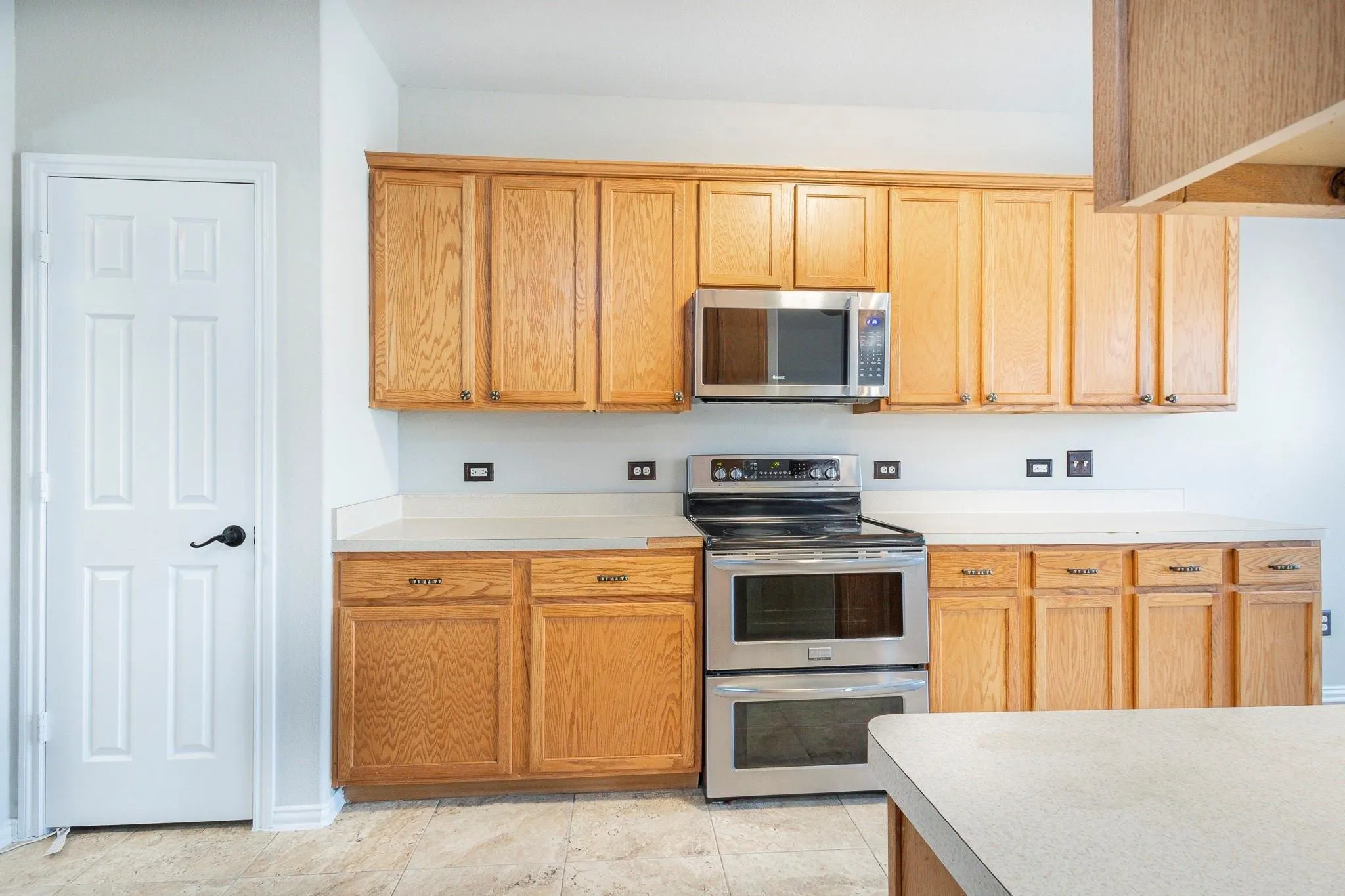 Wood-finish cabinetry, stainless steel microwave, stainless steel double oven range, light-toned countertop, and light-toned tile flooring
