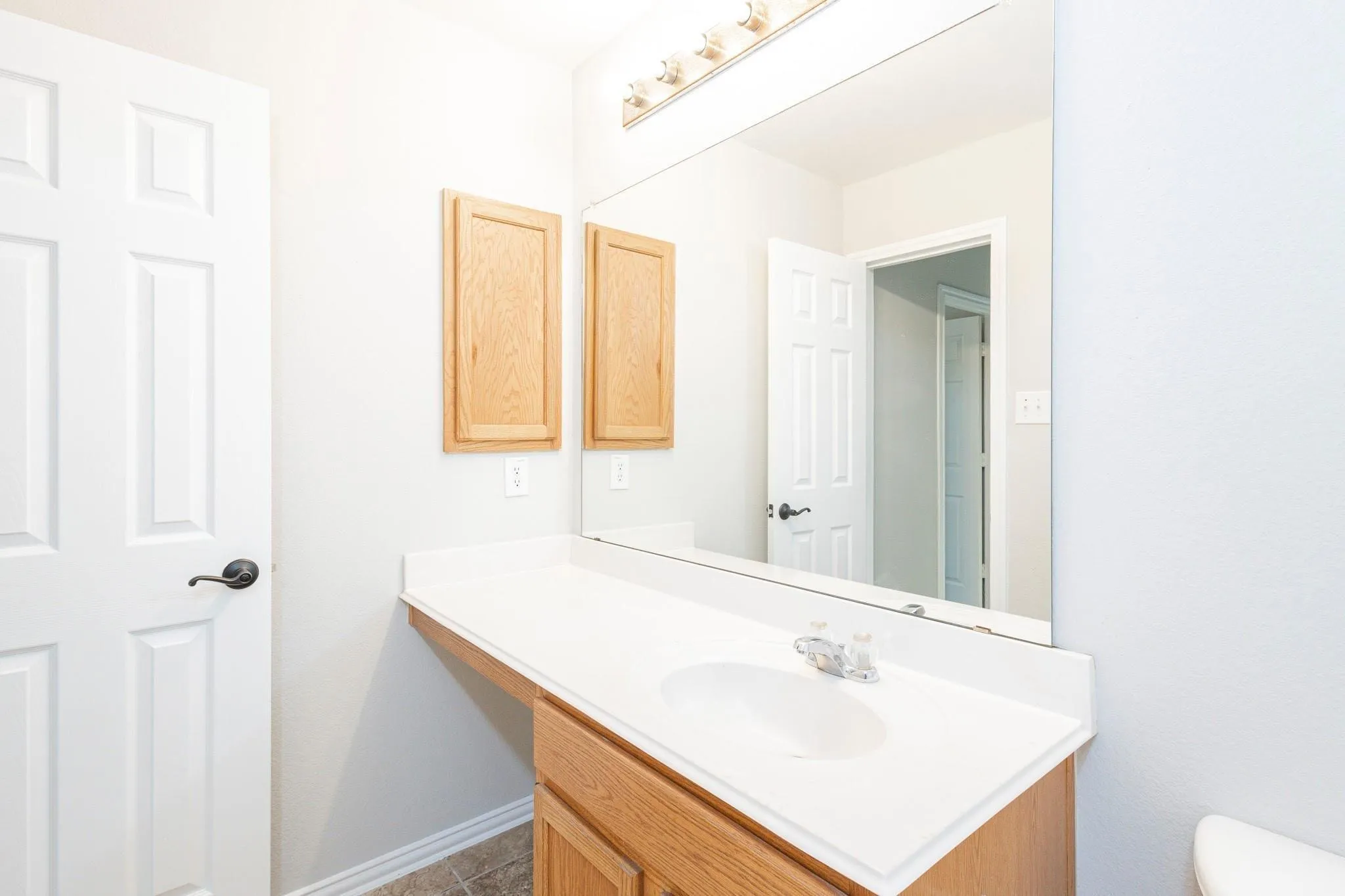 Vanity with a single basin, white countertop, wood-finish cabinetry, and wall-mounted mirror
