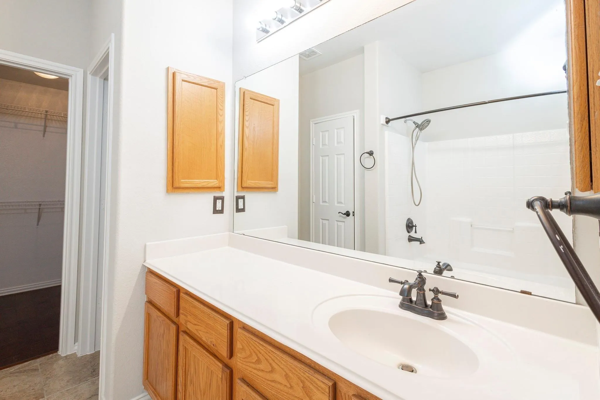 Single vanity with a light-toned countertop and built-in sink, wood-finish cabinetry, and a full-width mirror