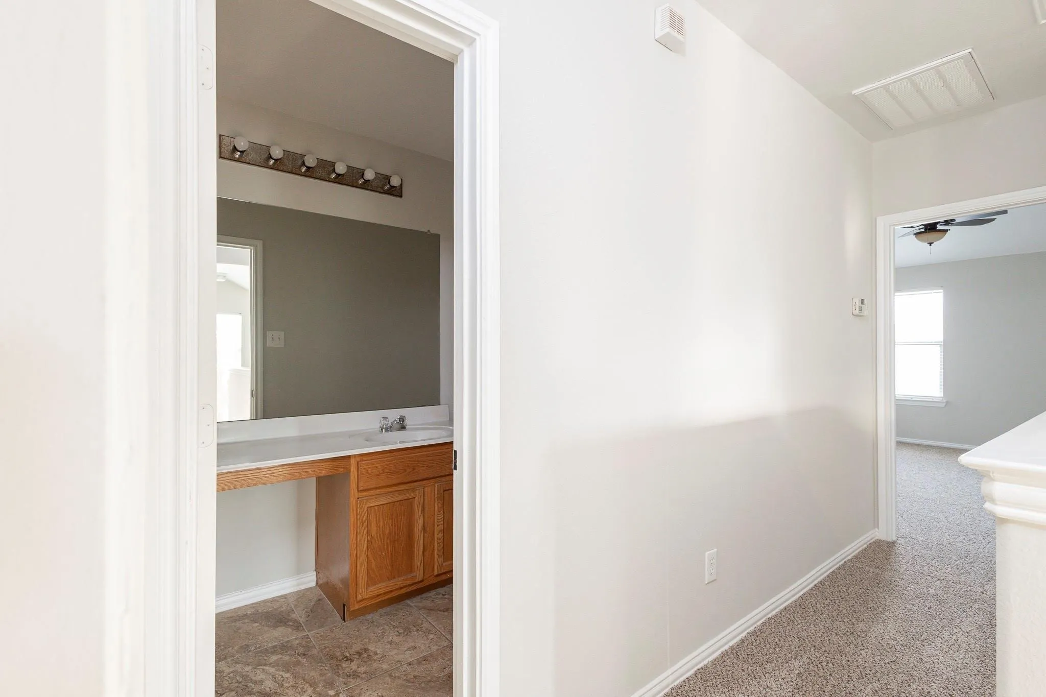 Bathroom vanity with wood-finish cabinetry, integrated sink, and wall-mounted mirror with overhead lighting
