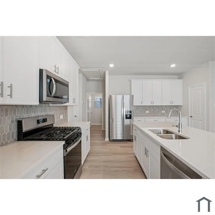Modern kitchen featuring white cabinetry, stainless steel appliances, light-toned wood-finish flooring, a kitchen island with an undermount sink, and a tiled backsplash