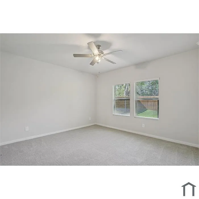 Soft gray wall paint, light gray carpeting, two windows with blinds, and a ceiling fan with integrated lighting