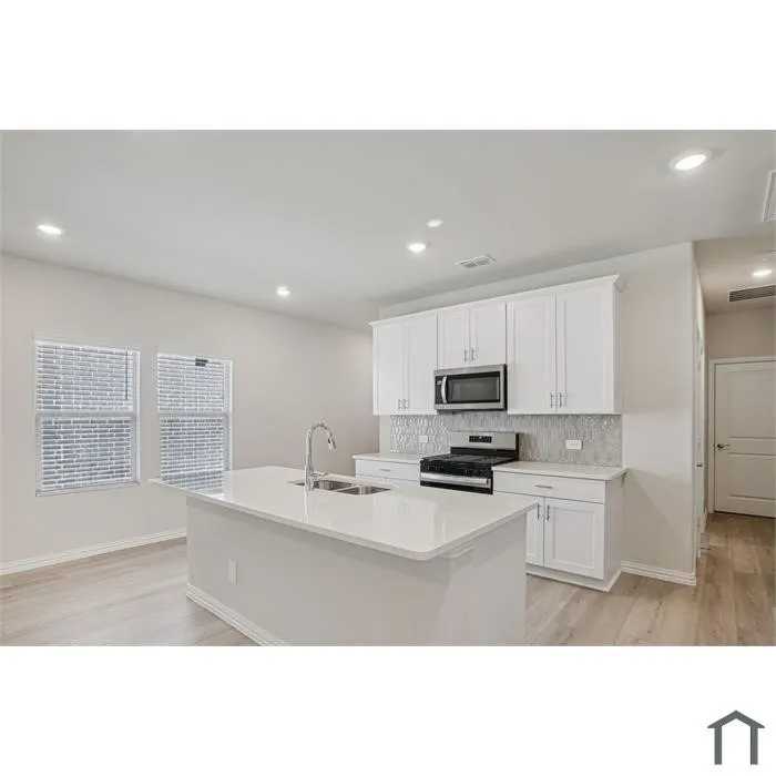 Kitchen featuring white shaker cabinetry, stainless steel appliances, a tile backsplash, wood-finish flooring, and a central island with a sink