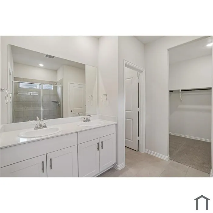 Double vanity with white cabinetry and chrome hardware, large unframed mirror, tiled flooring, and a walk-in shower with glass enclosure