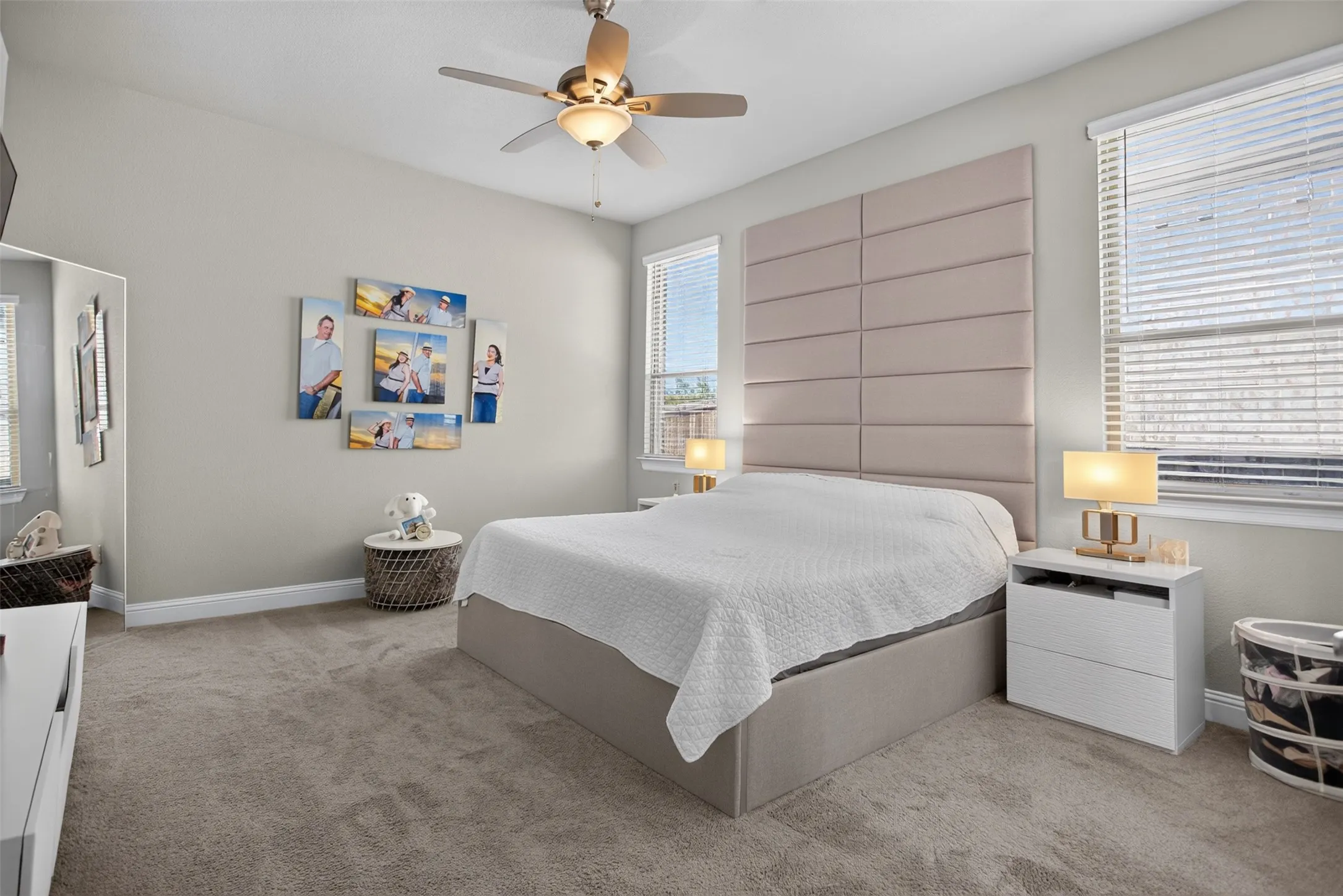 Plush carpet flooring, multiple windows with blinds, ceiling fan with integrated lighting, and a neutral color palette