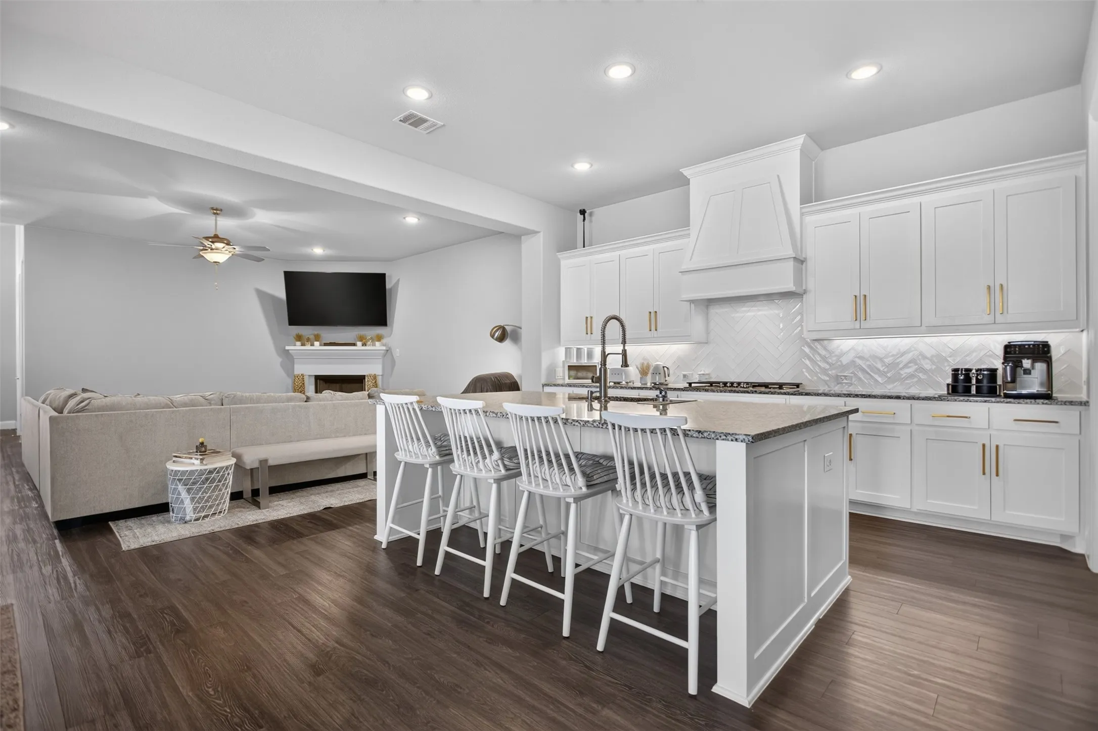 Kitchen island with counter seating, white cabinetry, herringbone tile backsplash, and dark wood-finish flooring