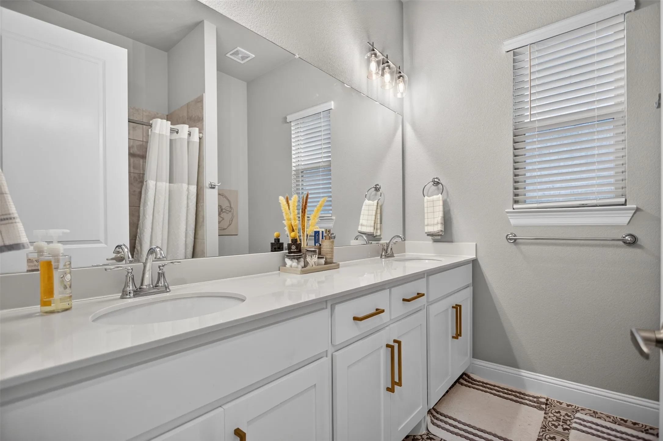 Dual undermount sinks with chrome fixtures, white cabinetry with gold-tone hardware, and a large vanity mirror