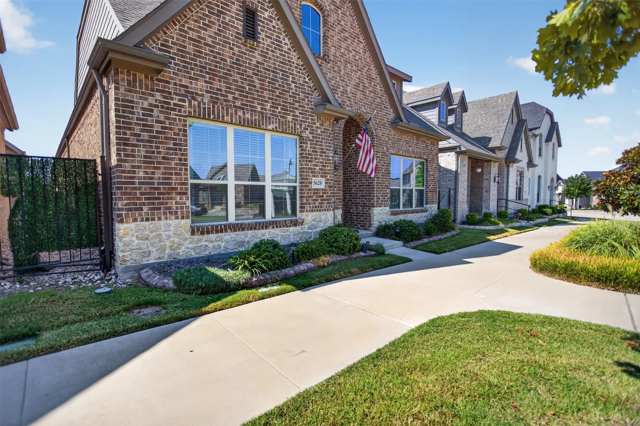 Brick and stone facade with arched entry, gabled roofline, and established landscaping