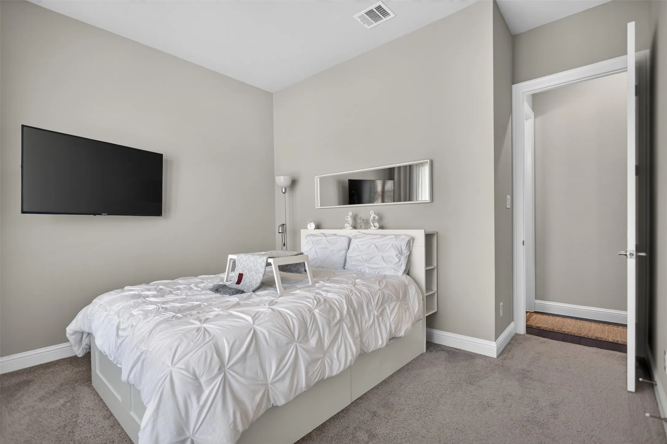 Wall-mounted television, neutral wall paint, carpeted flooring, and white trim