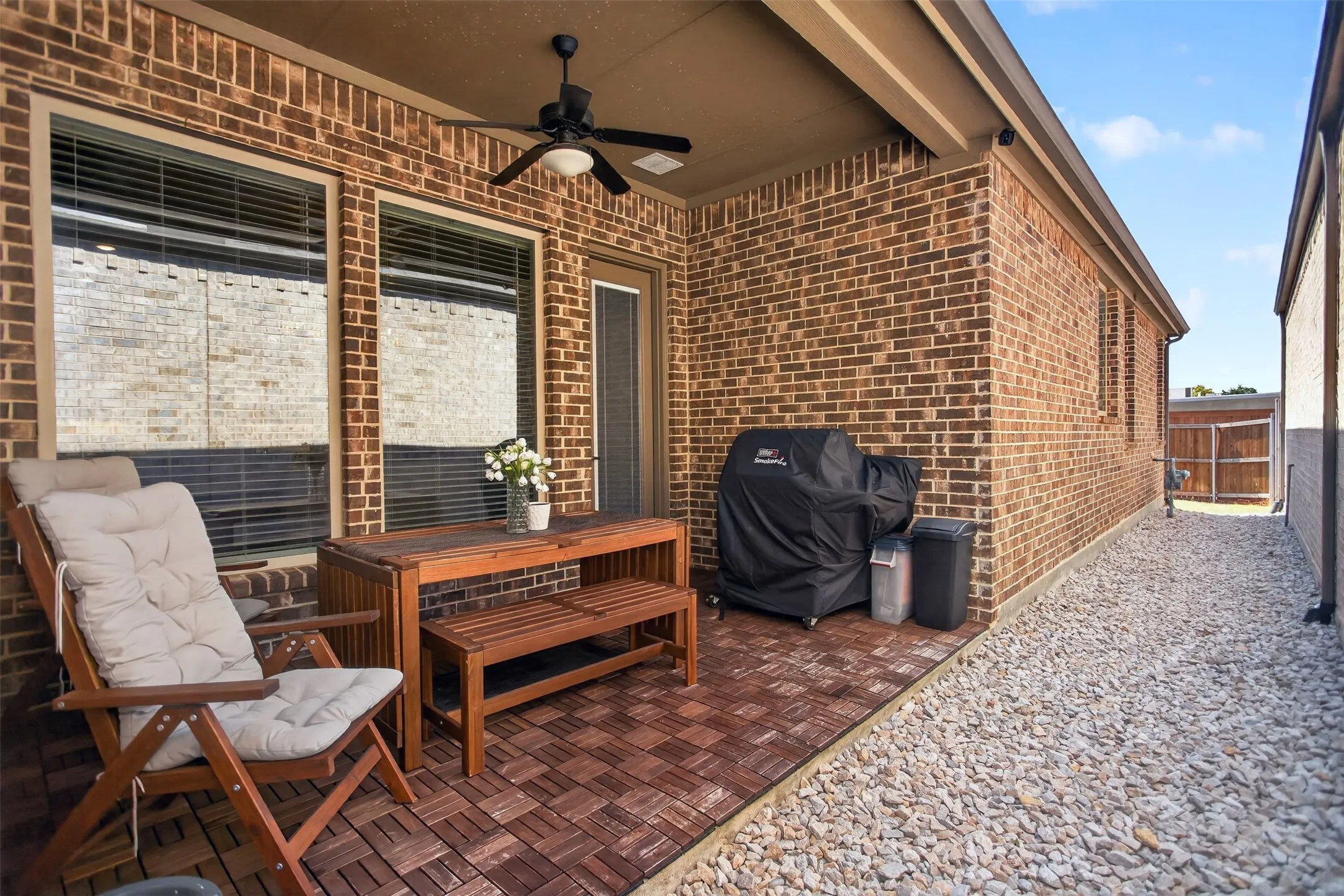 Covered patio featuring brick exterior, wood-finish tile flooring, ceiling fan, and a gravel pathway