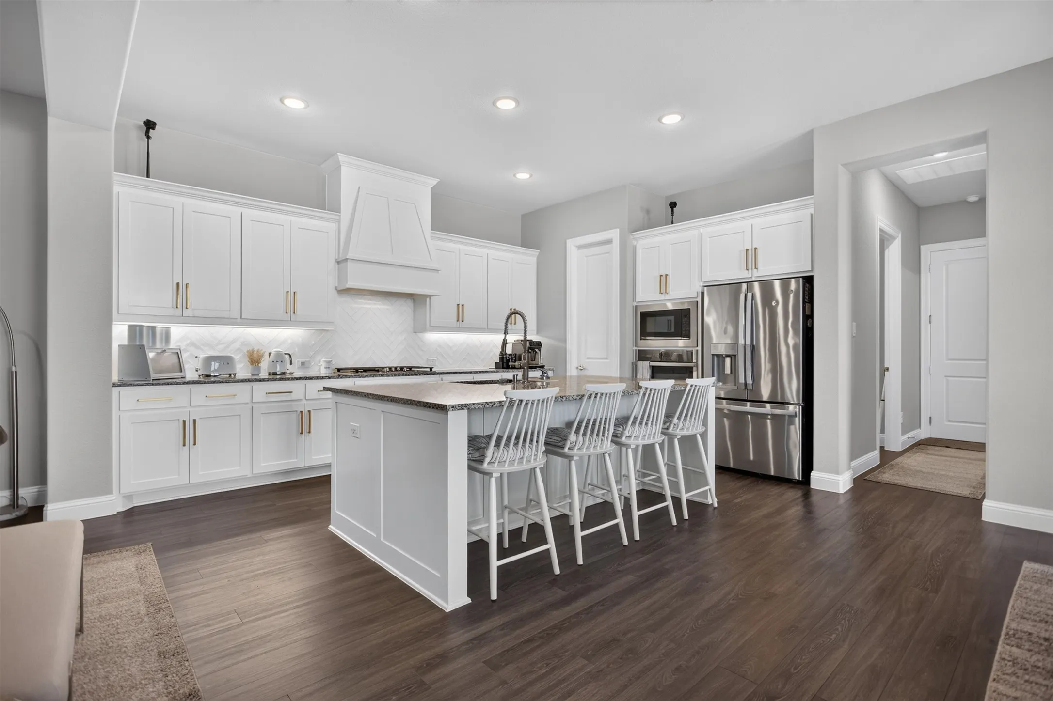 Kitchen featuring white cabinetry, stainless steel appliances, a center island with seating, dark wood-finish flooring, and recessed lighting
