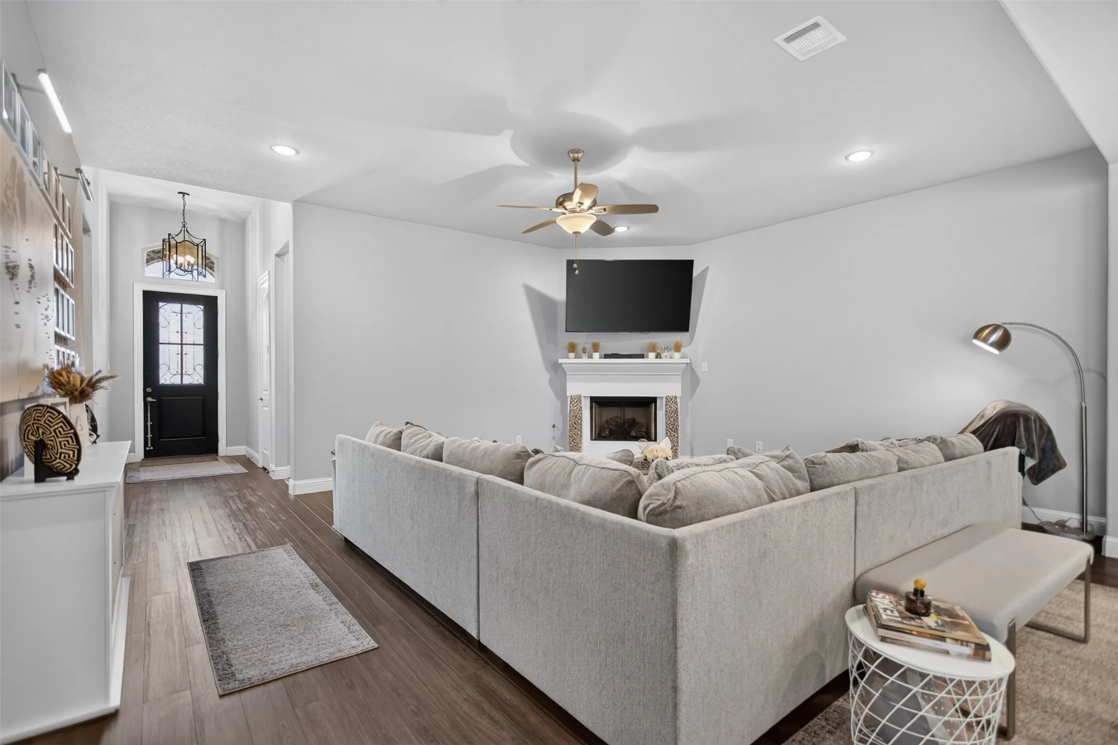 Spacious living area featuring wood-finish flooring, a ceiling fan, recessed lighting, and a fireplace with a decorative mantel
