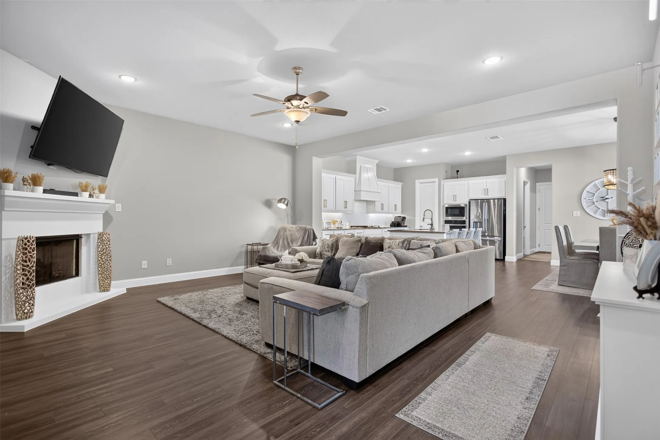 Open-concept living space with dark wood-finish flooring, a corner fireplace, and a ceiling fan