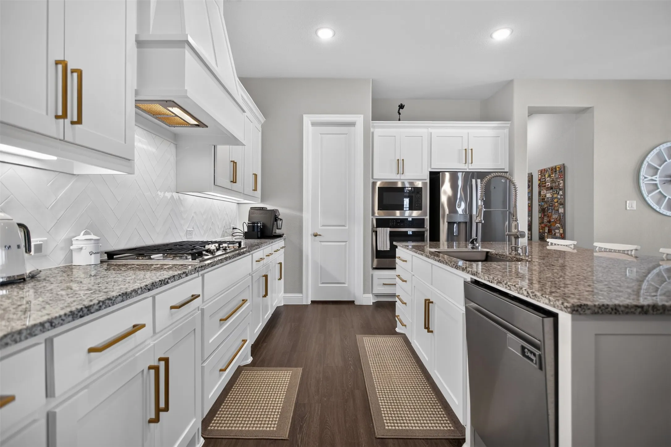 White cabinetry with gold-tone hardware, granite countertops, stainless steel appliances, wood-finish flooring, and recessed lighting