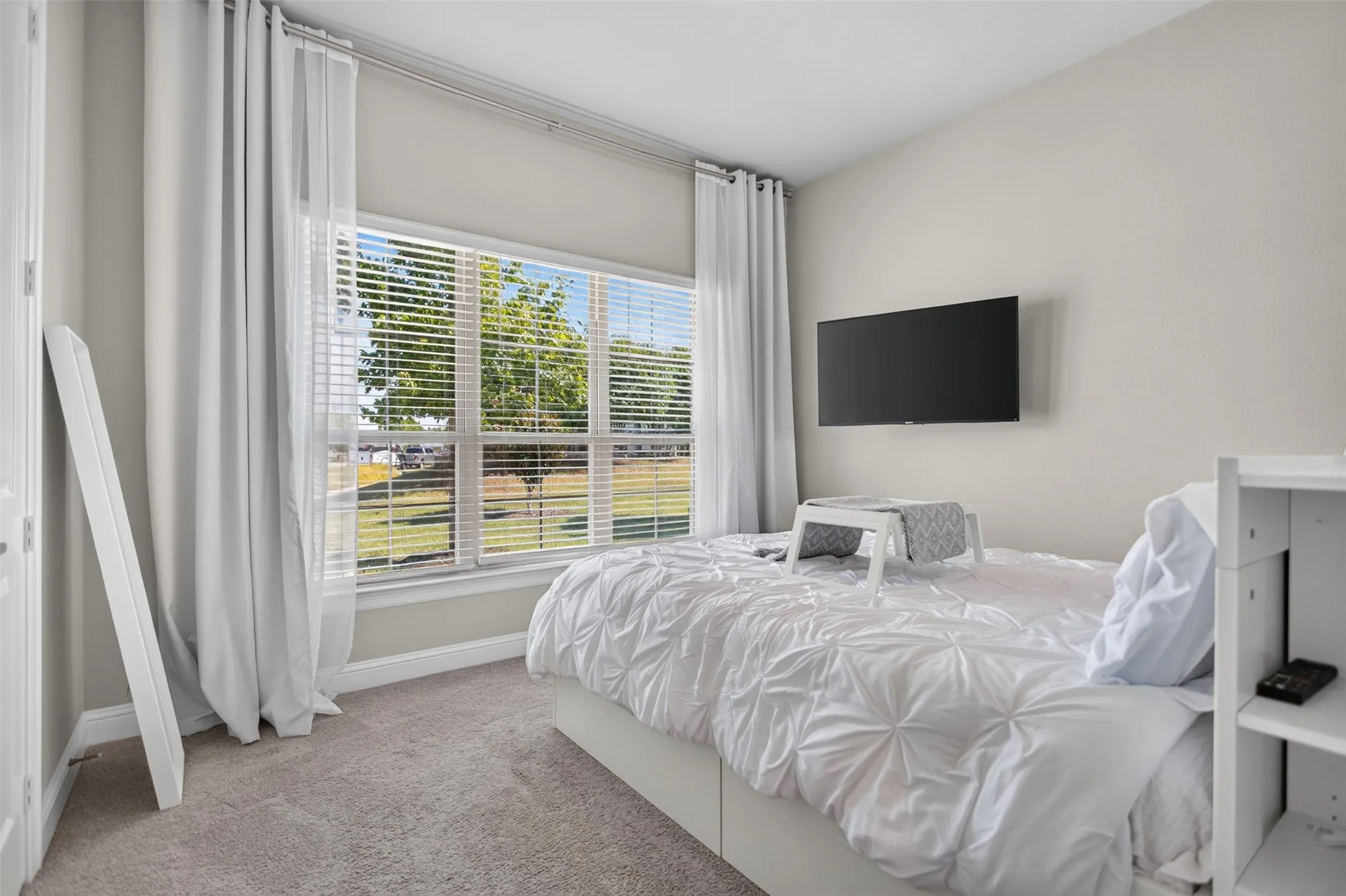 Wall-mounted television with a large window featuring blinds and full-length drapes