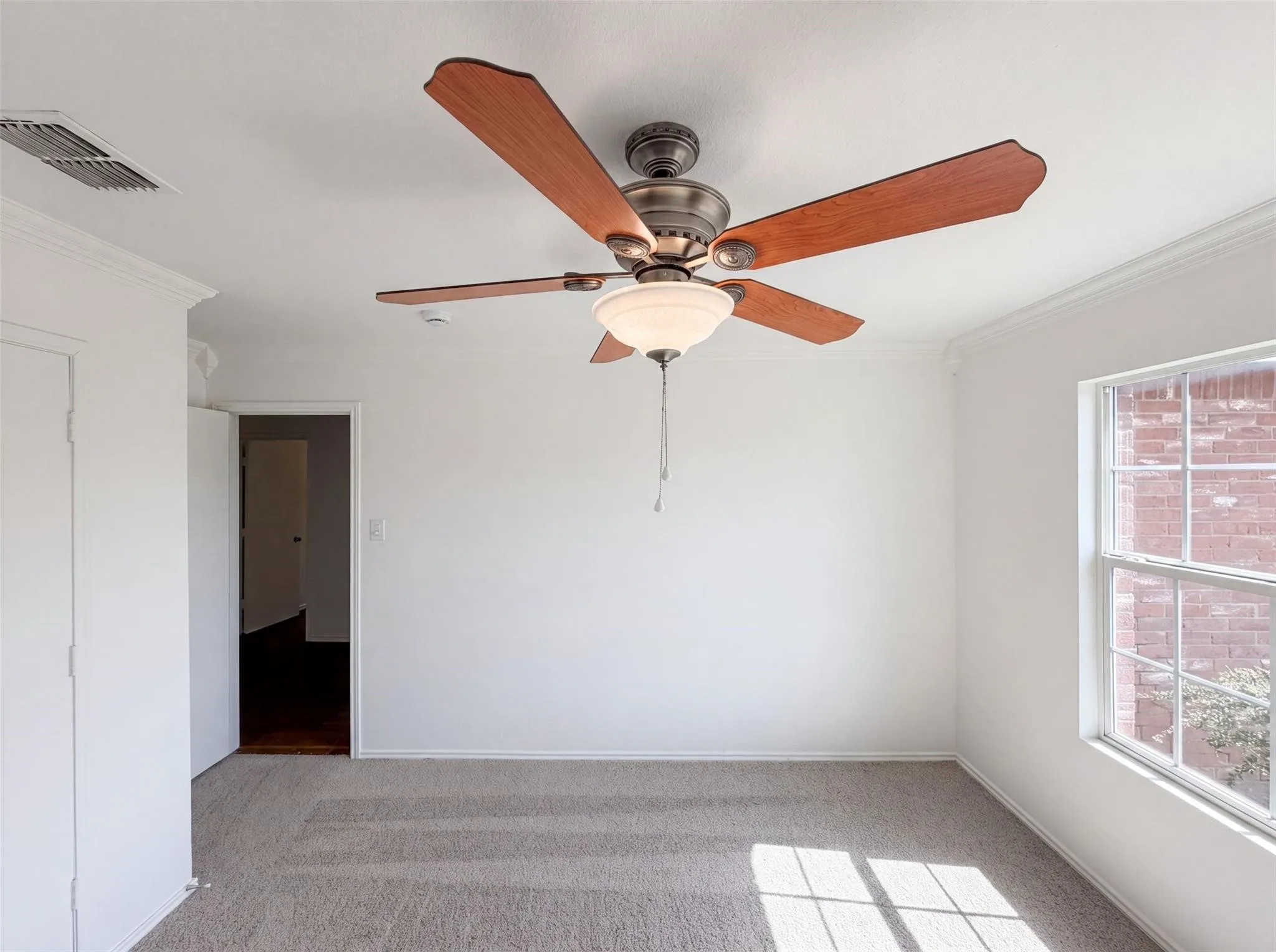 Crown molding, ceiling fan with light fixture, carpeted flooring, and a multi-pane window