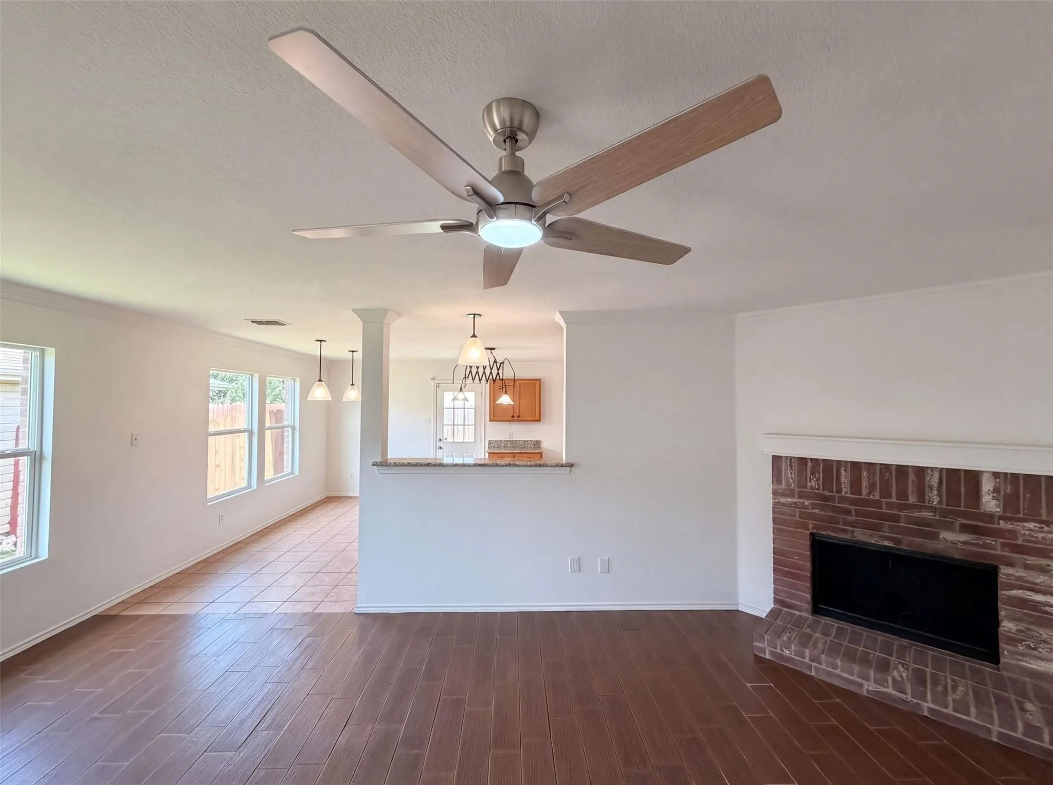 Spacious interior featuring wood-finish flooring, a brick fireplace with mantel, and a ceiling fan